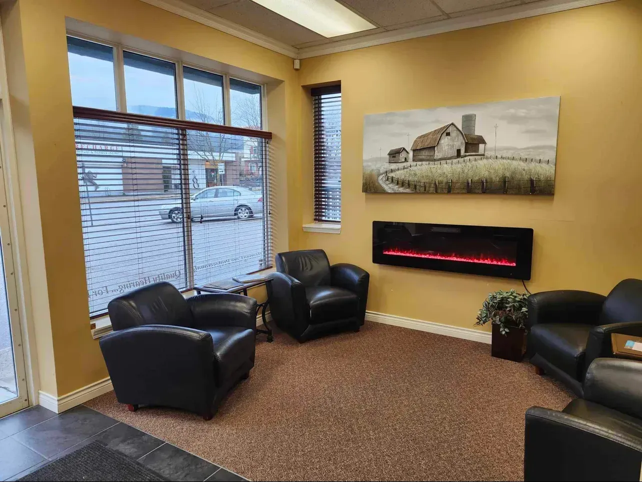 Waiting area with black leather chairs, fireplace, artwork, and window with blinds.