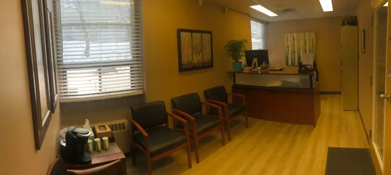 Waiting room with chairs, a desk, and a window with blinds.
