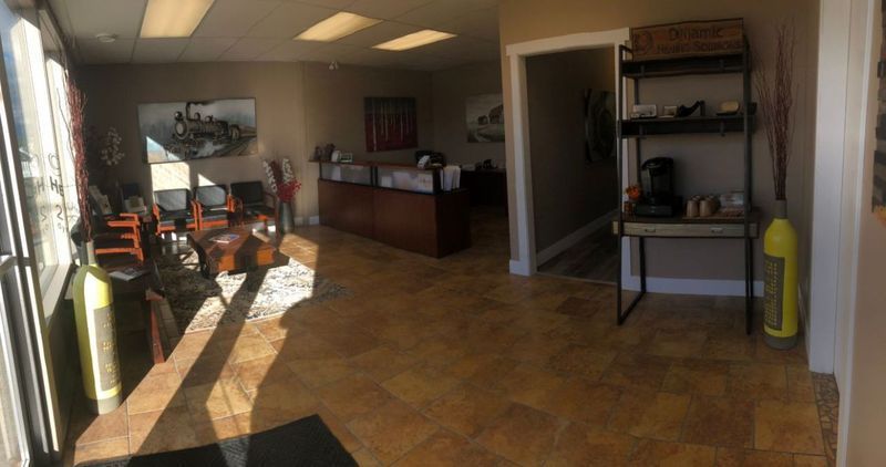 Reception area with tiled floor, reception desk, waiting area, and shelving unit. Sunlight streams in.
