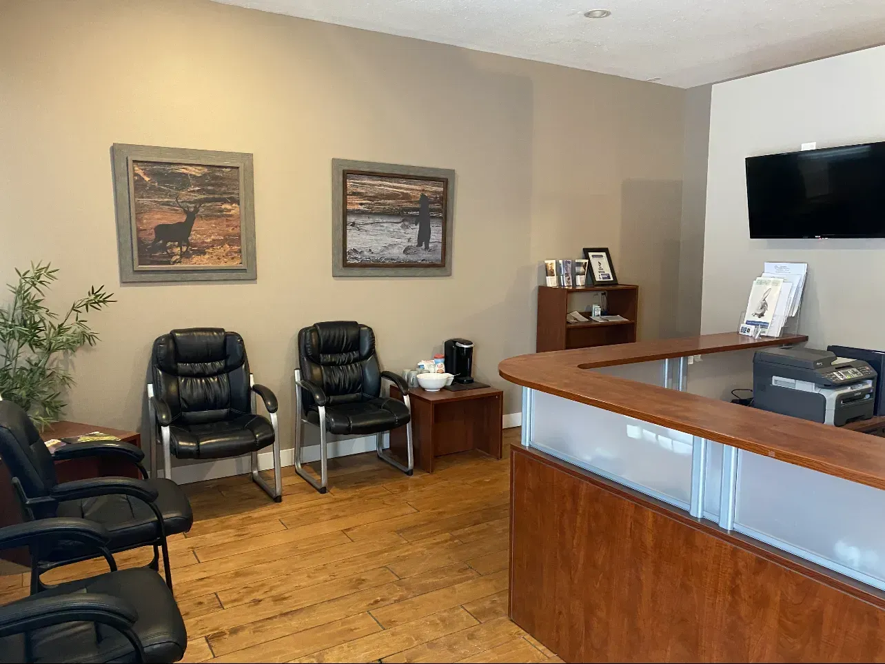 Waiting room with chairs, art, and a reception desk. Wood floors, neutral walls, and a flat-screen TV.