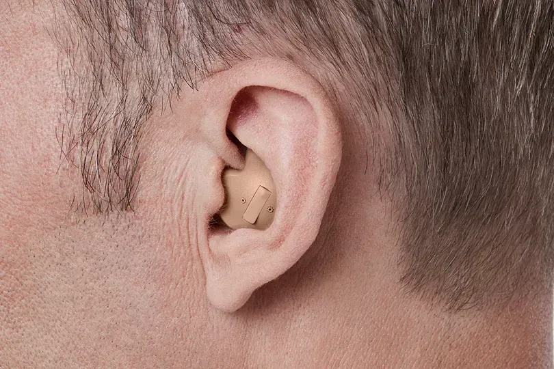 Close-up of a person's ear with a beige hearing aid inside the ear canal.