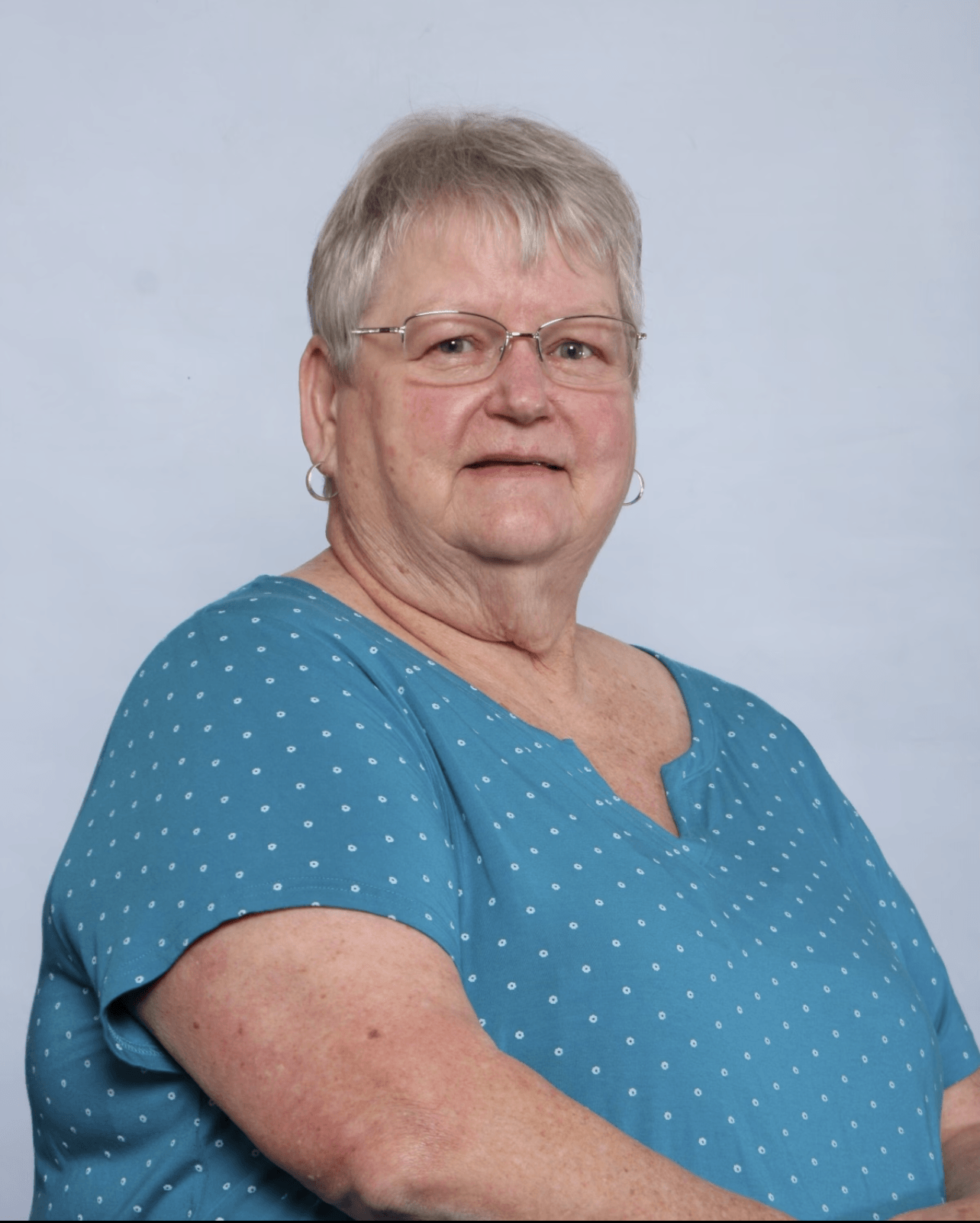 Woman with glasses wearing a blue polka-dot shirt, smiling against a light blue backdrop.