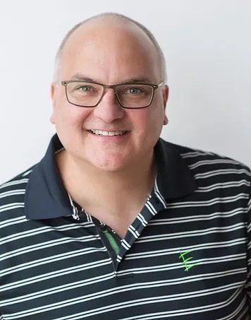 Man wearing glasses and striped polo shirt smiles at camera.