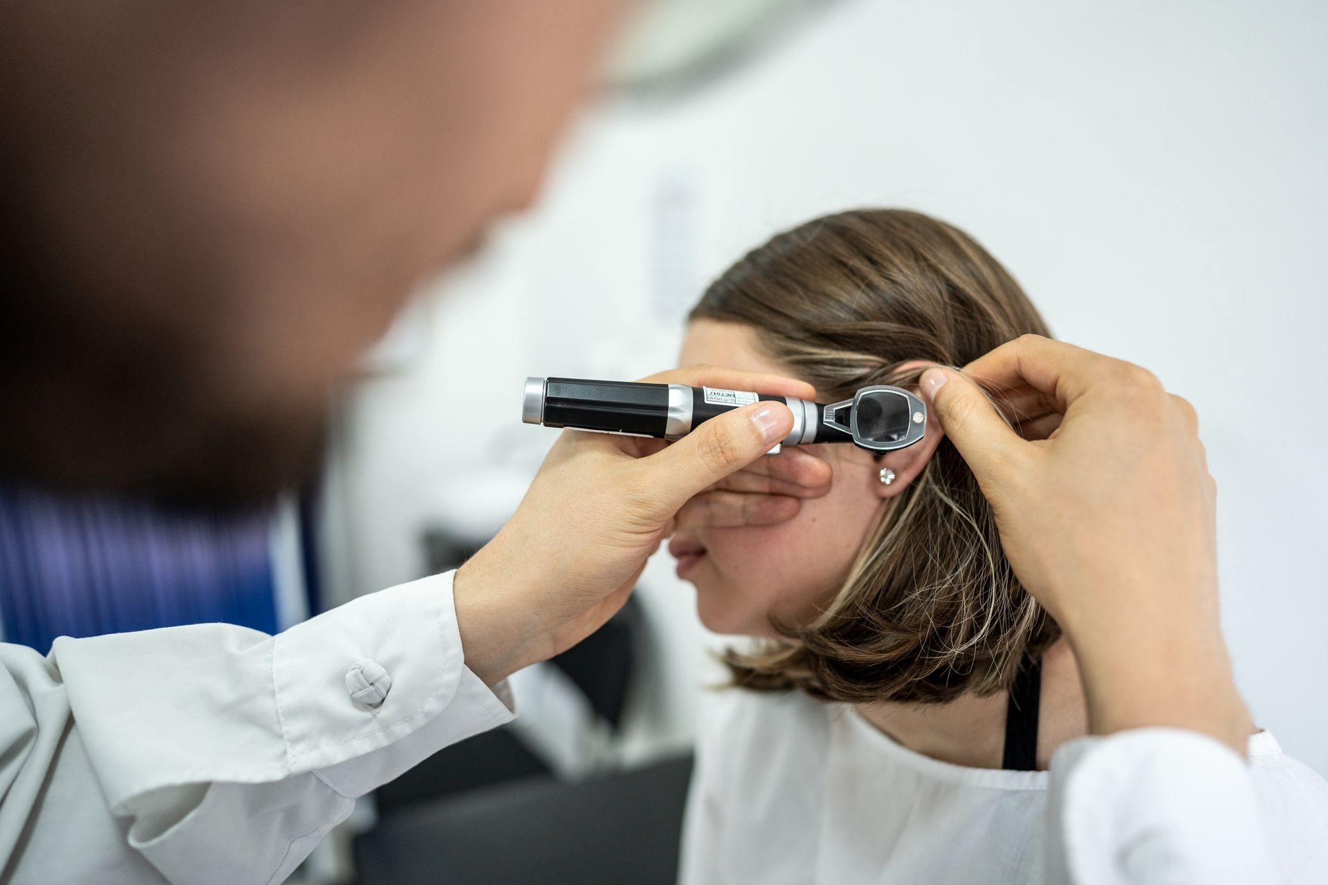 Doctor examining a person's ear with an otoscope in a clinical setting.