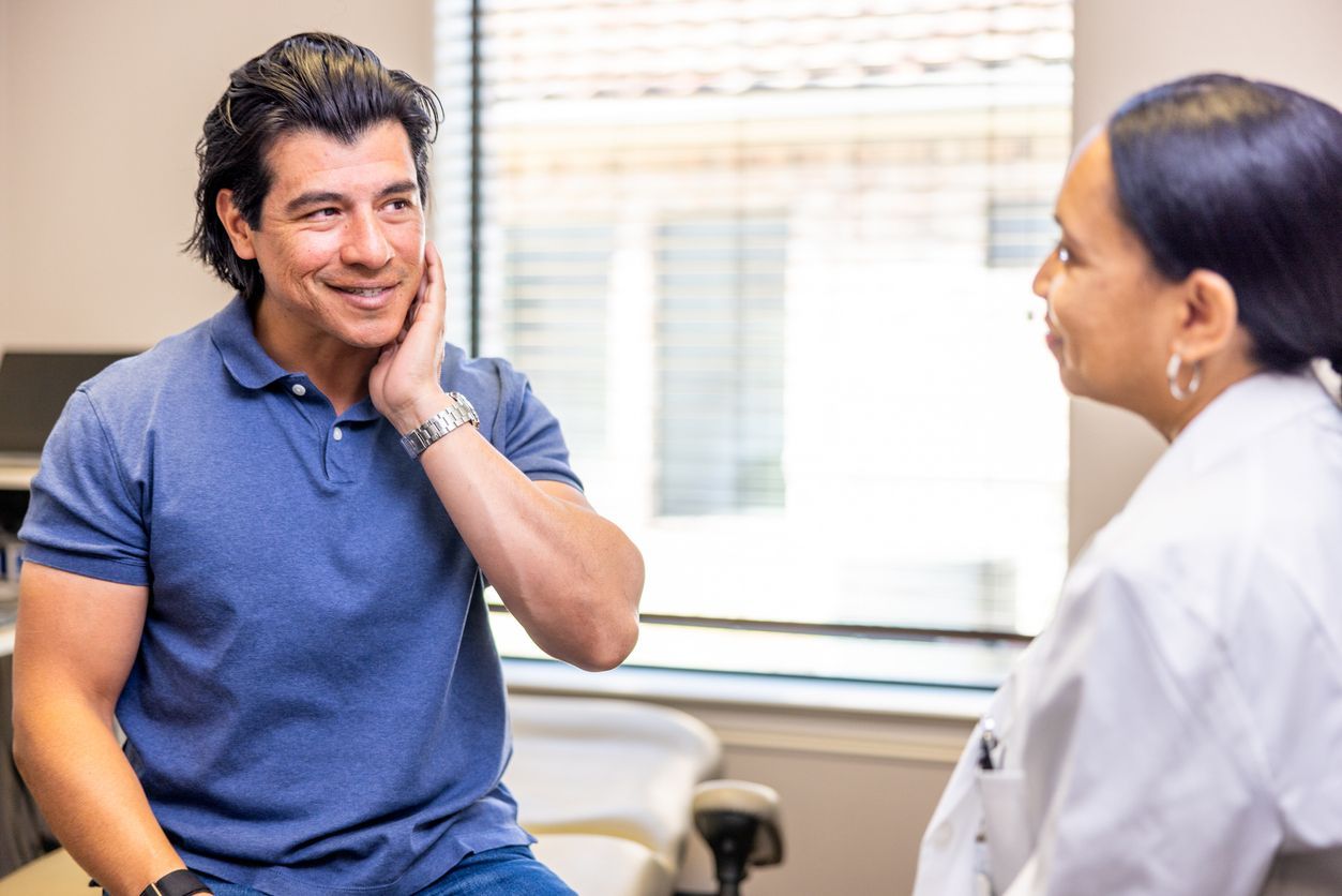 Man in blue shirt, touching cheek, talking to doctor in white coat in an office.