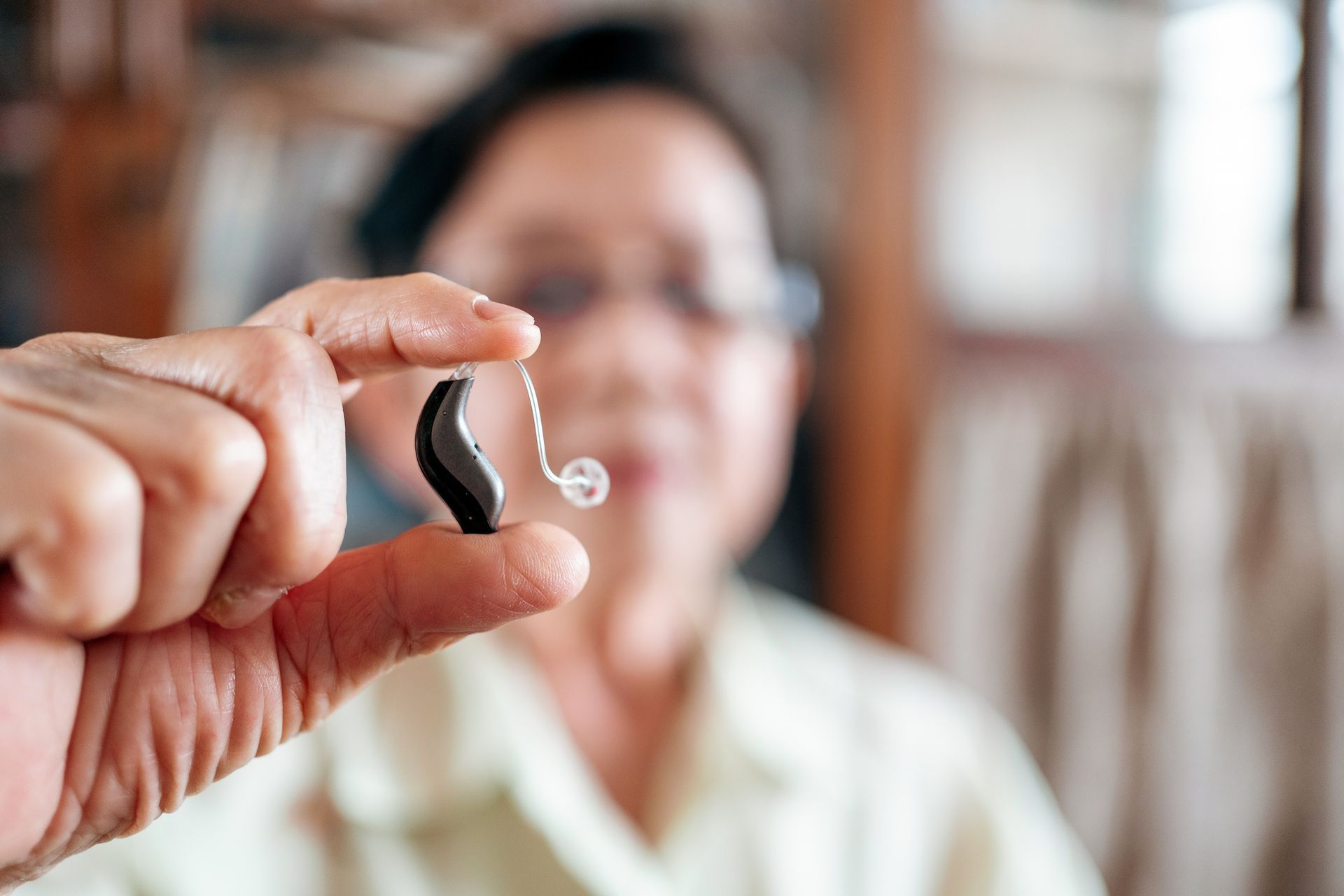 Person holding a small black hearing aid with clear tubing; blurred background.