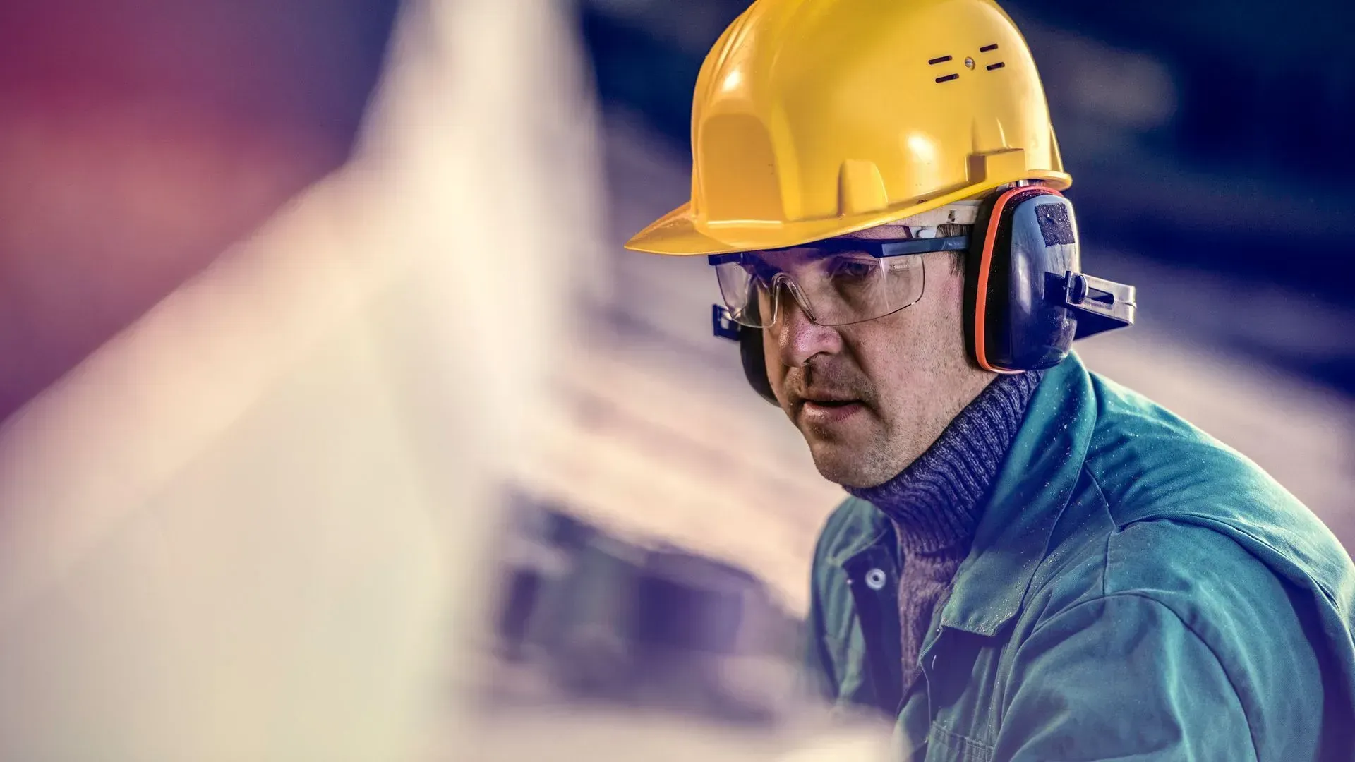 Worker wearing a yellow hard hat, safety glasses, and ear protection in a construction setting.
