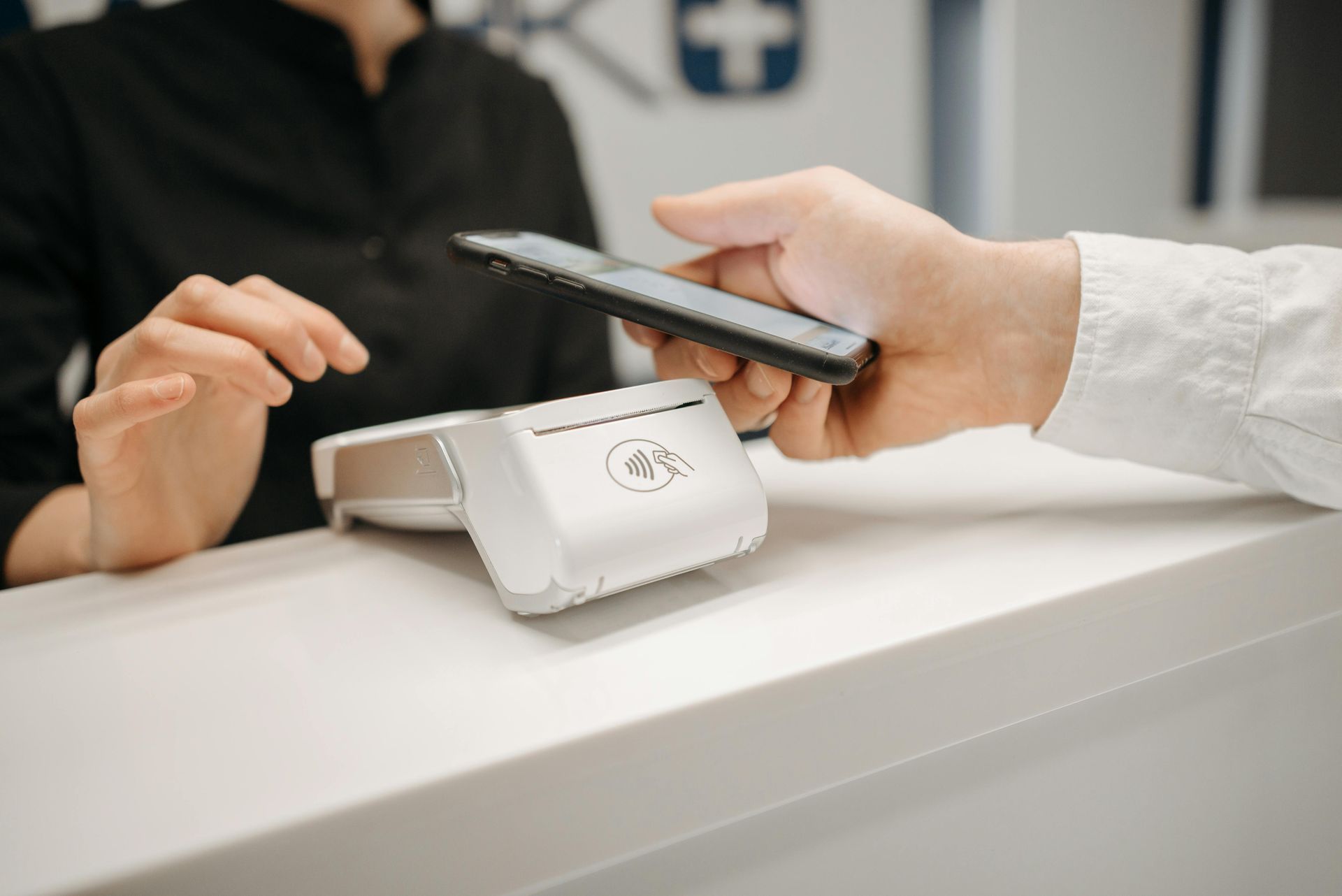 Person paying with phone at a payment terminal on a white counter.