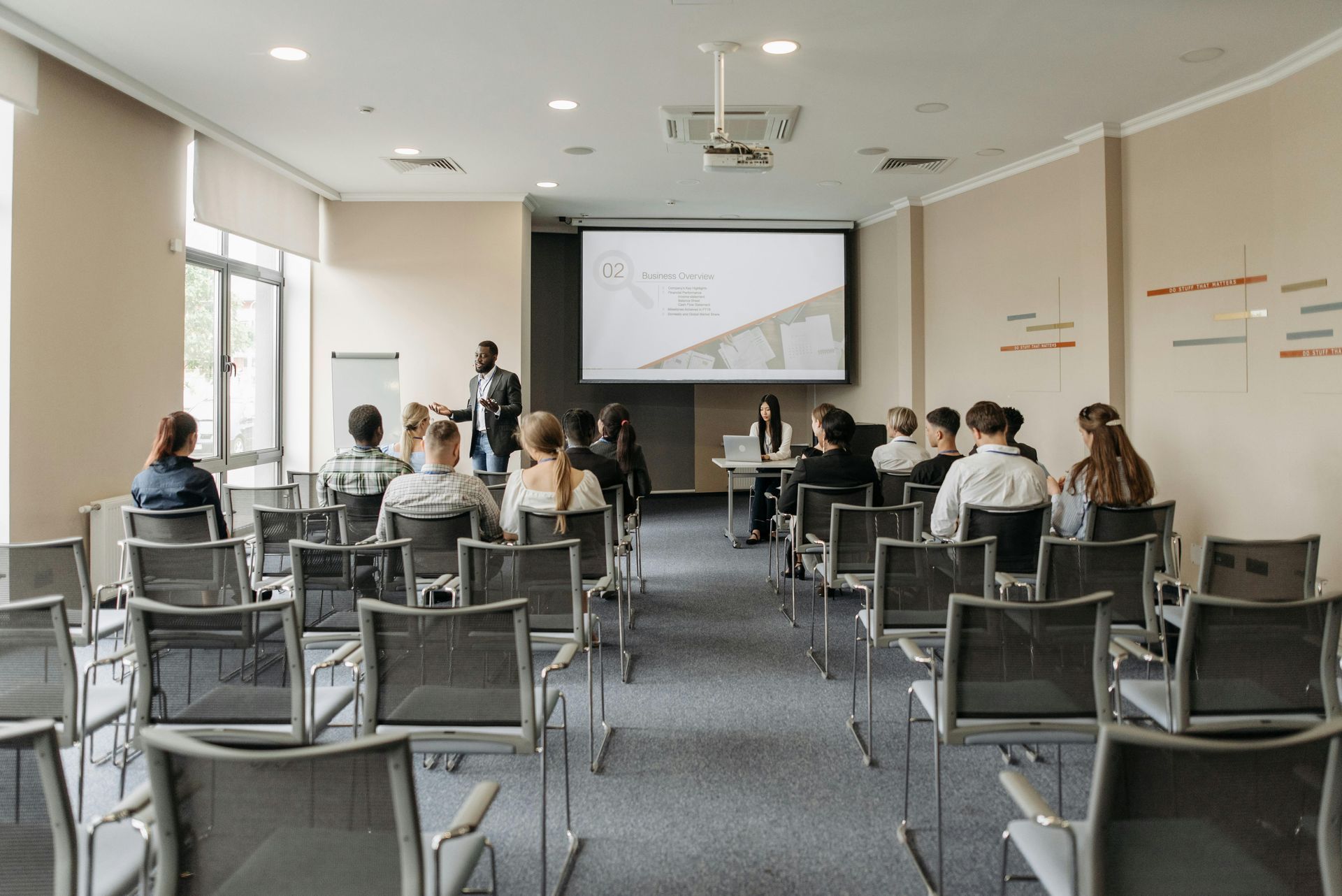 A presentation in a conference room with a presenter and an audience seated in chairs.