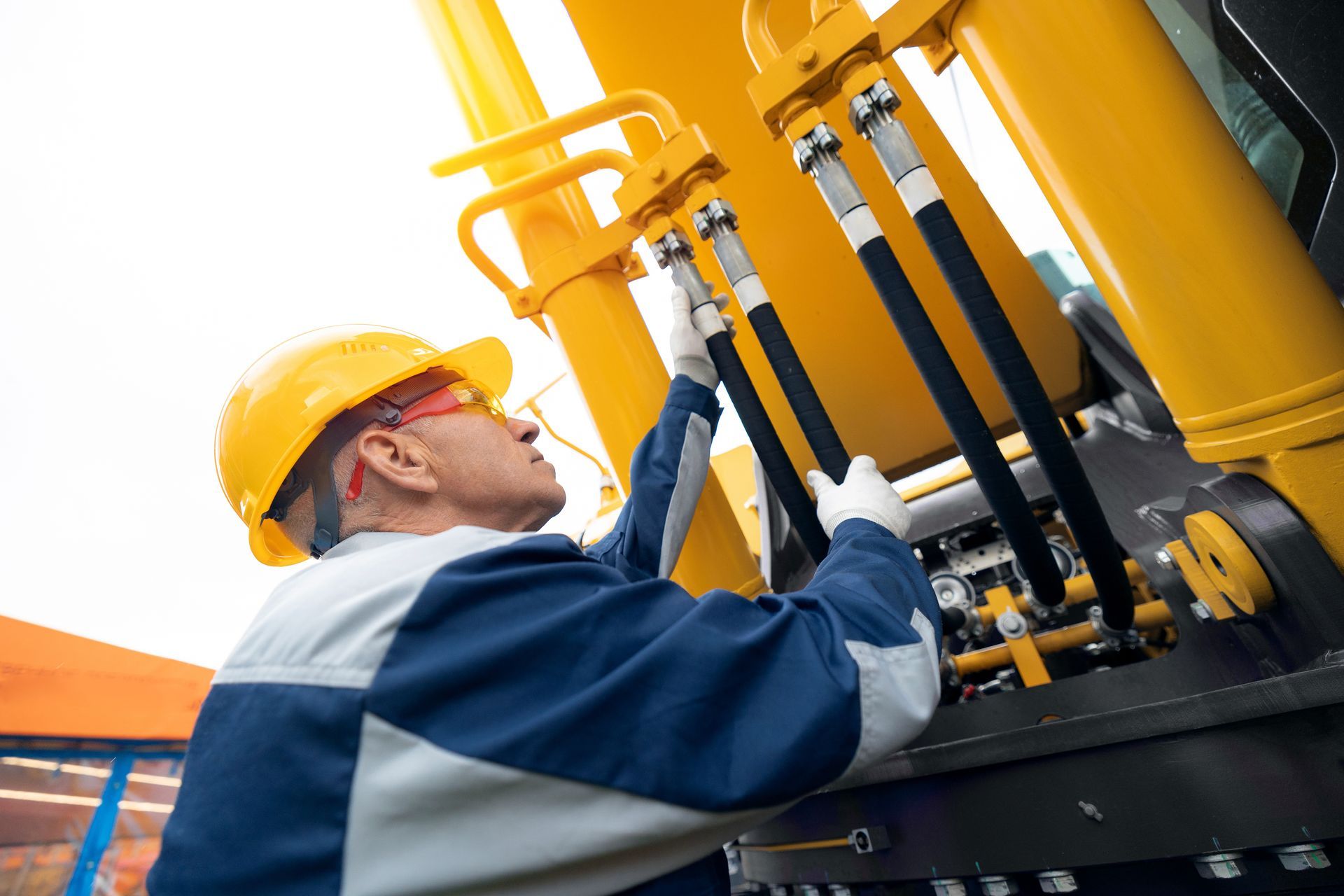 A worker in a hard hat inspects hydraulic machinery, ensuring safe and precise operation.