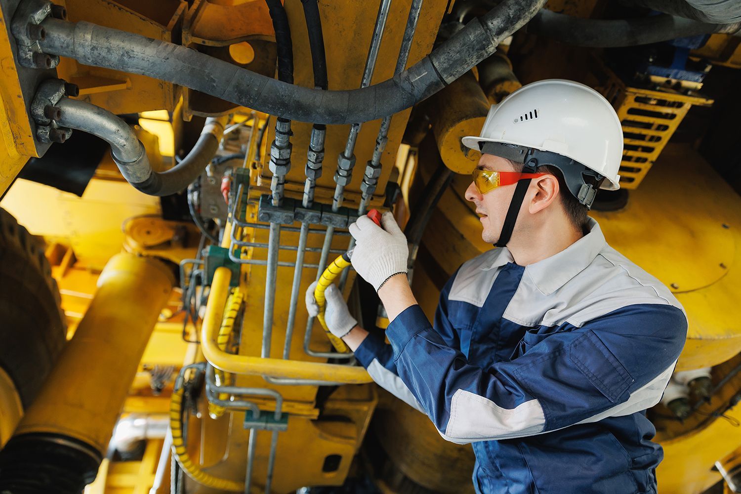 worker mechanic inspecting hydraulic hose of mining truck in garage.