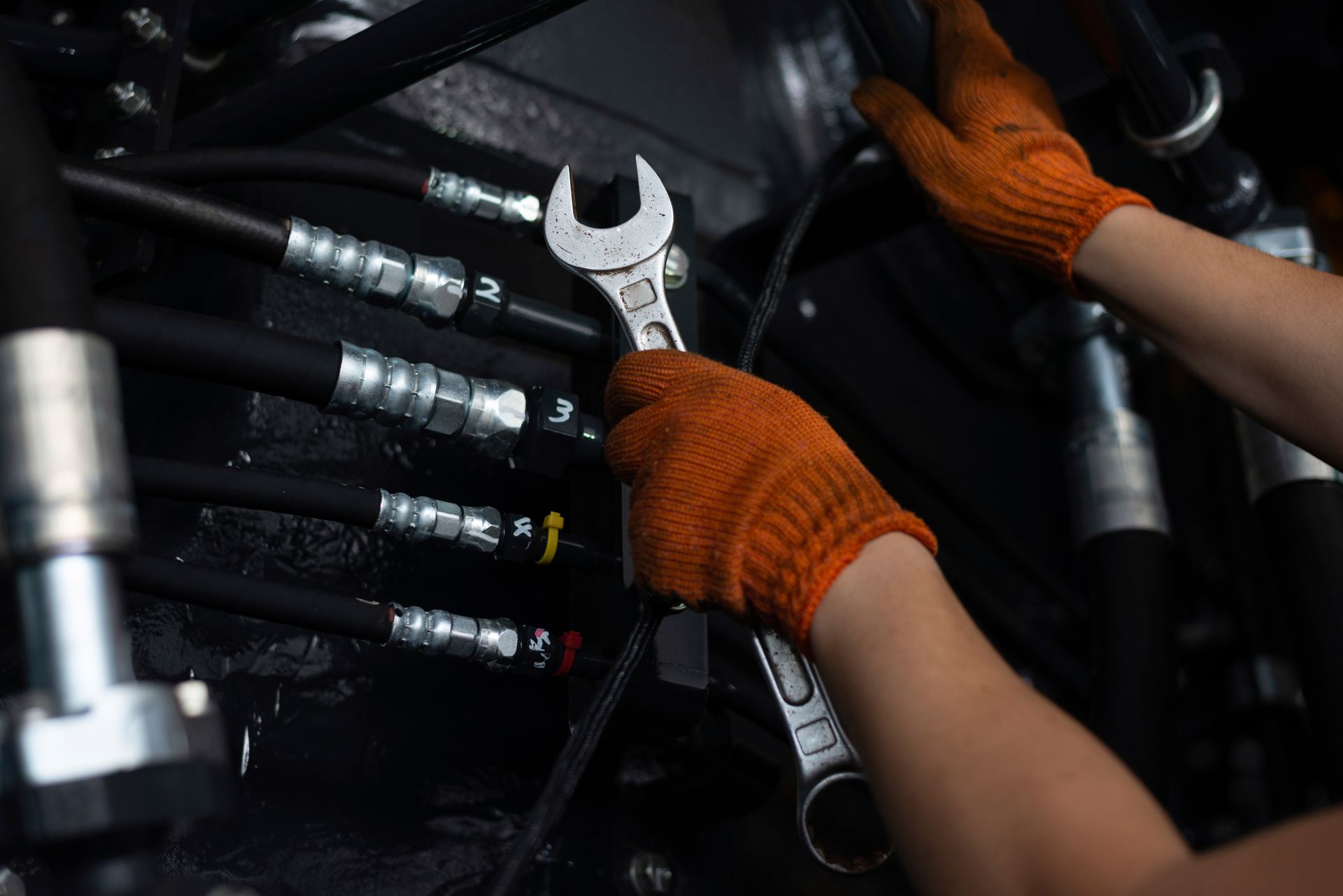 Hands in orange gloves tightening a wrench on black hoses and fittings.