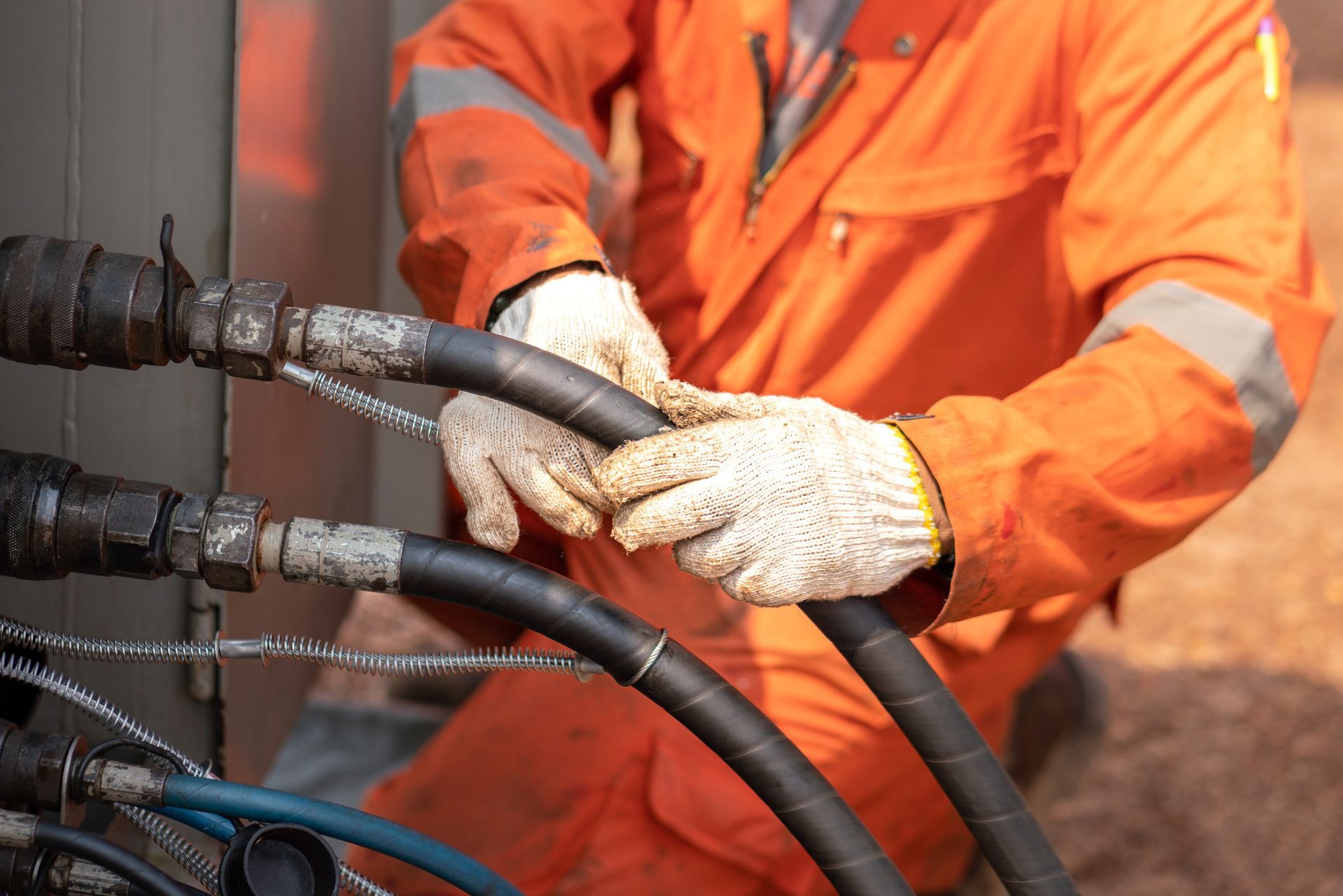 Person in orange work coveralls and gloves connecting black hoses.