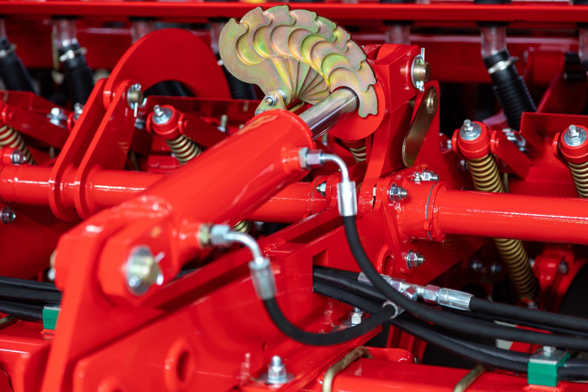 Close-up of red farm machinery with hydraulic cylinders and a hinged section.