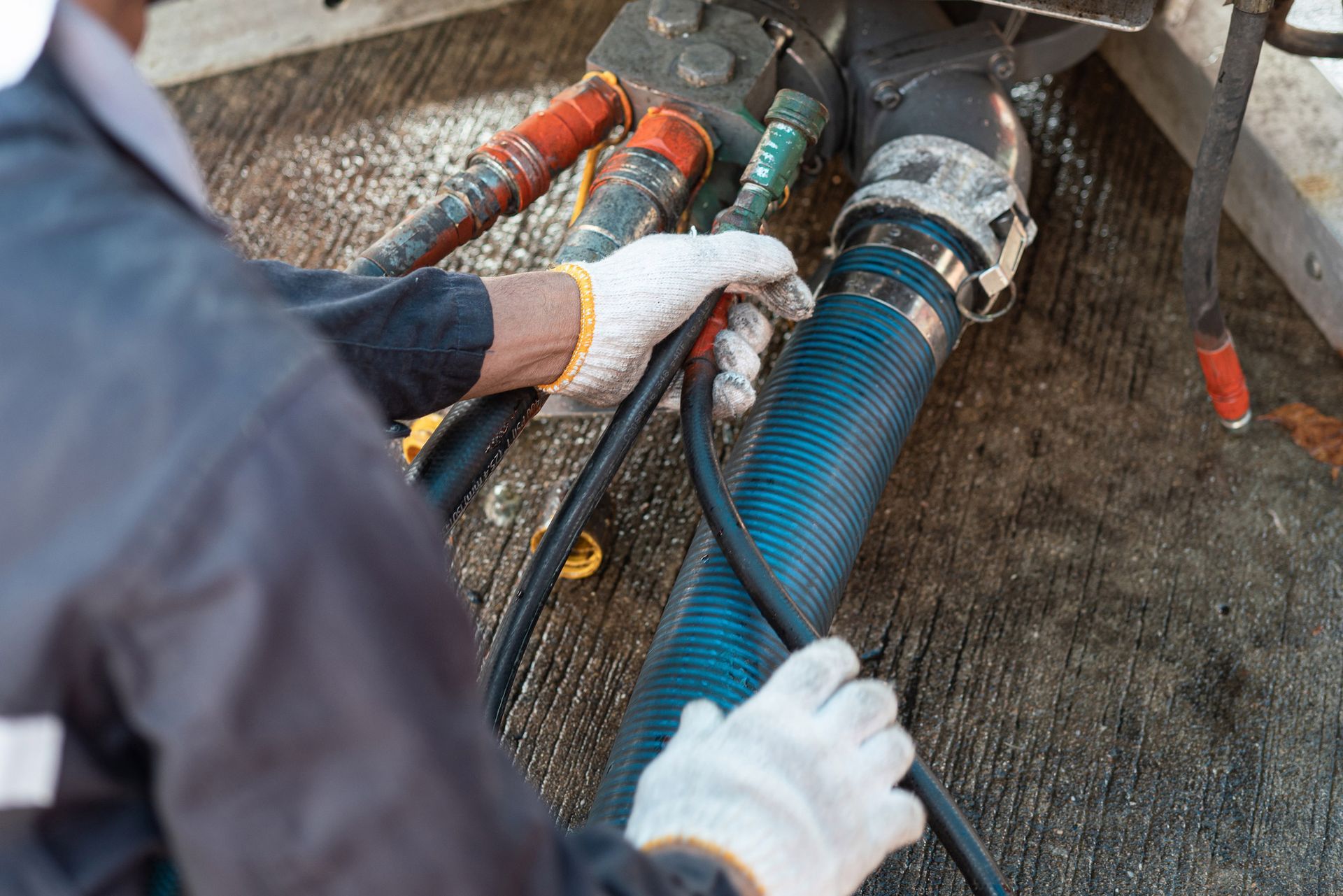 A person wearing gloves connecting hoses to a tanker truck.
