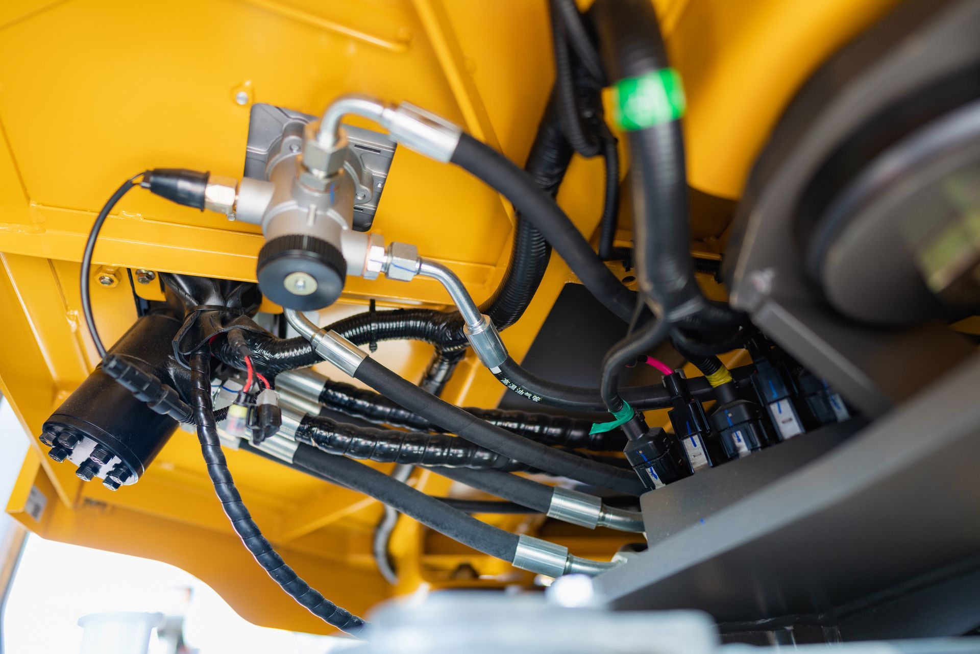 Yellow machinery interior with hydraulic hoses and valves.