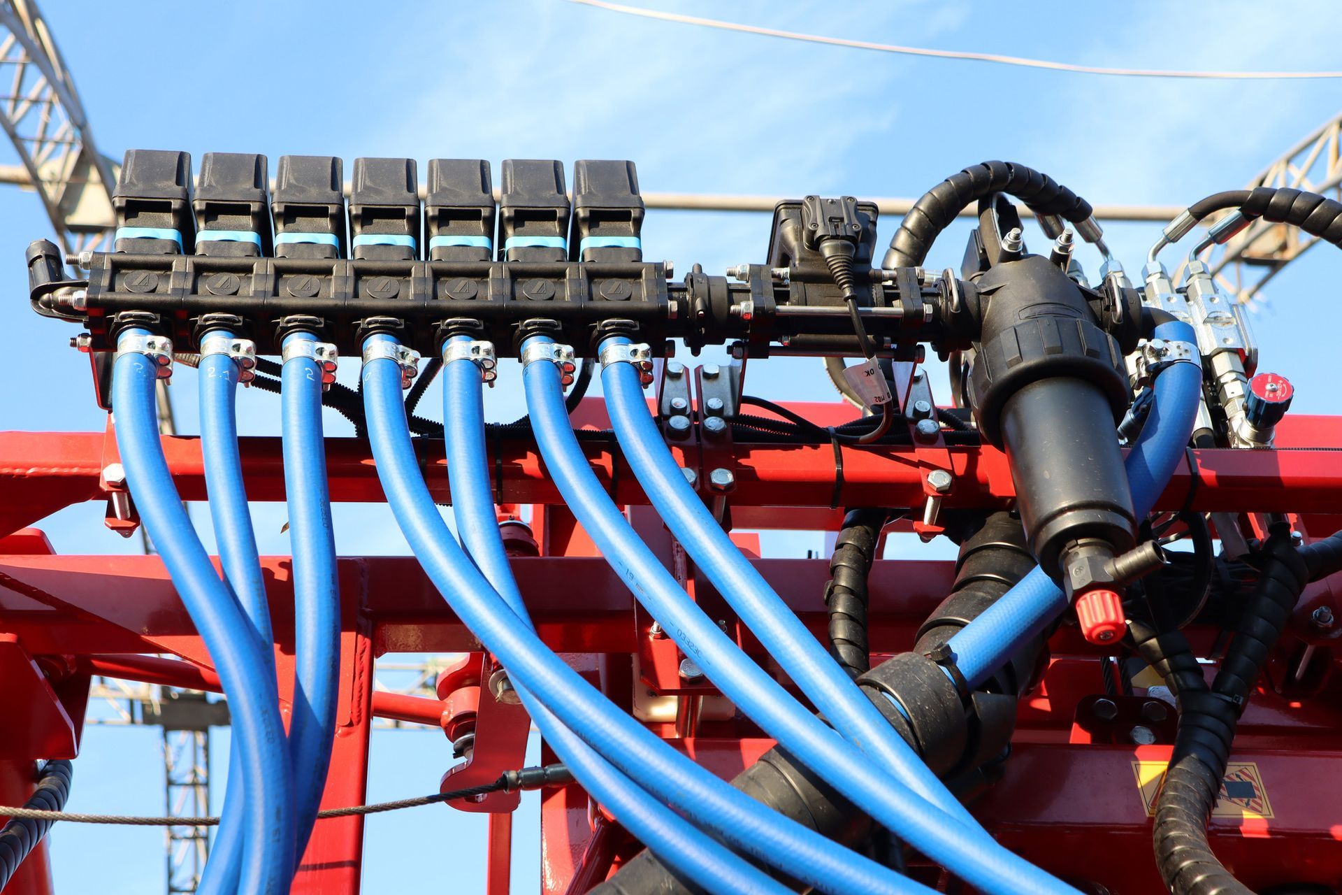 Blue hoses connected to a black manifold on a red agricultural machine.