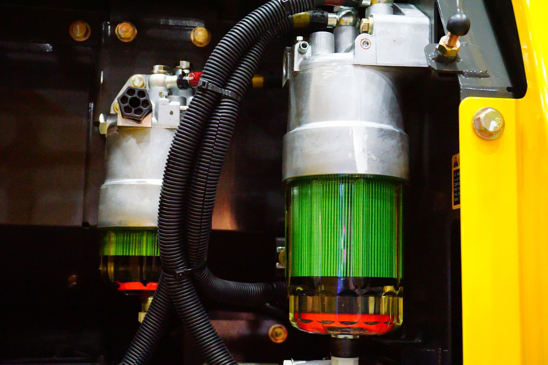 Two fuel filters with green filters visible inside, mounted on a yellow and black machine.