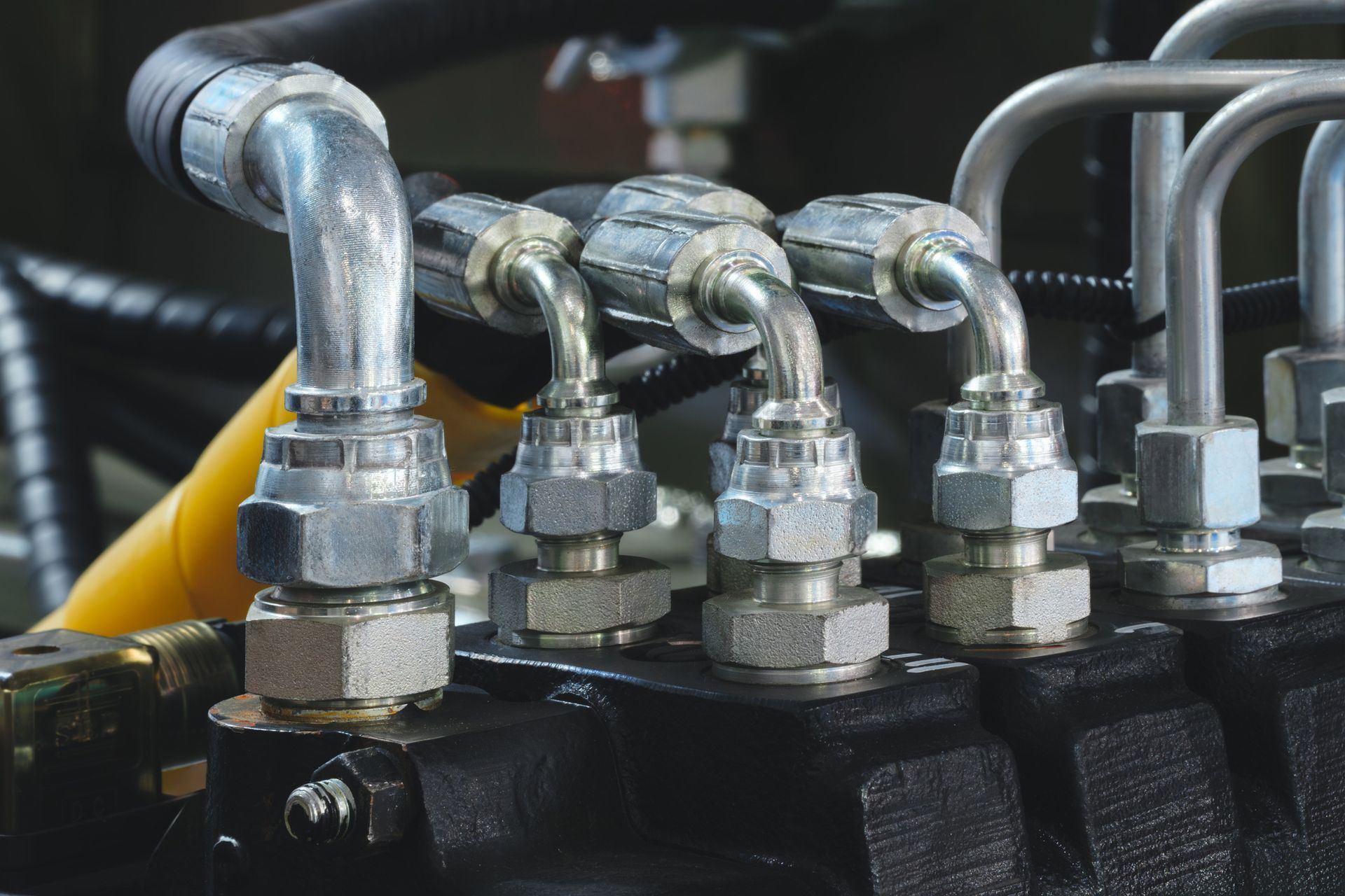 Close-up of hydraulic fittings with steel tubing and nuts, attached to a black machine component.