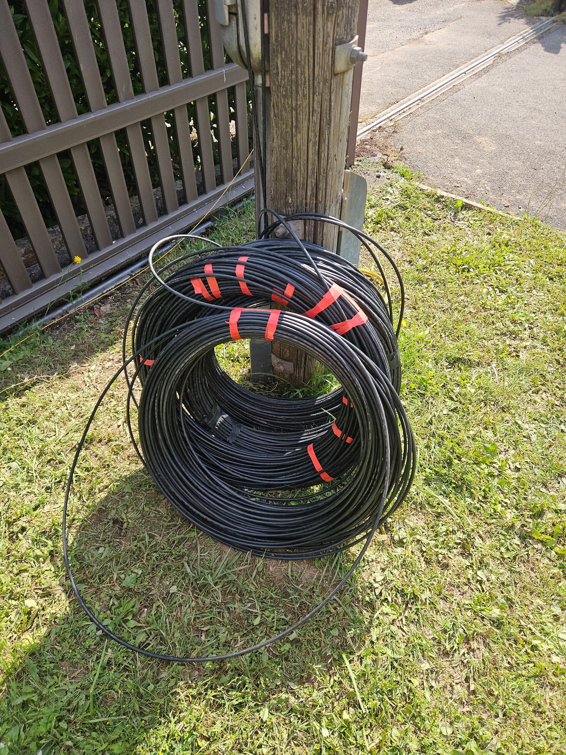Un tas de fils électriques sont posés sur l'herbe près d'une clôture