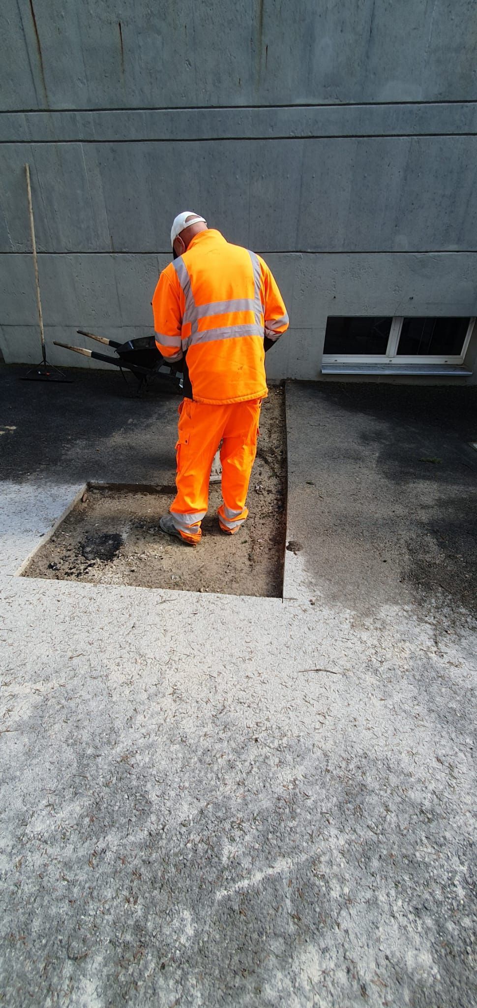 Un homme en salopette orange travaille sur une surface en béton