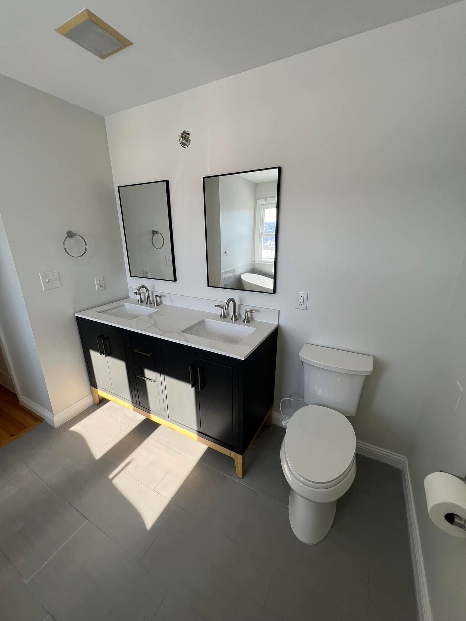 A bathroom with two sinks , a toilet and two mirrors.