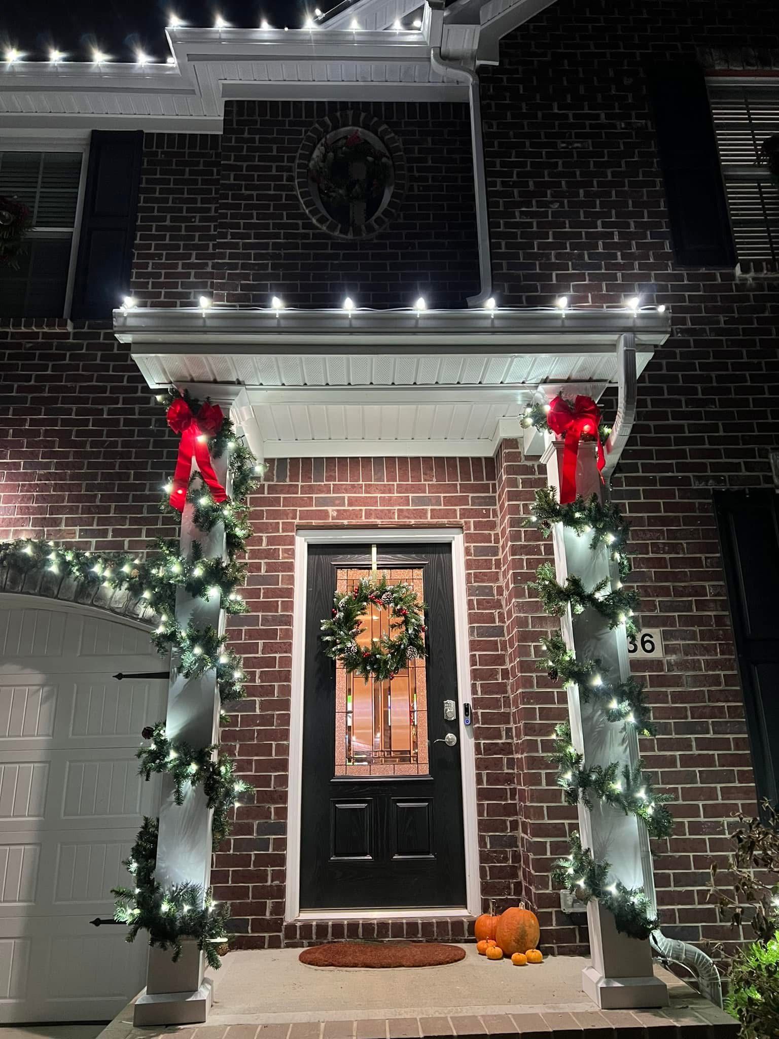 A brick house with a porch decorated for christmas with lights and pumpkins.
