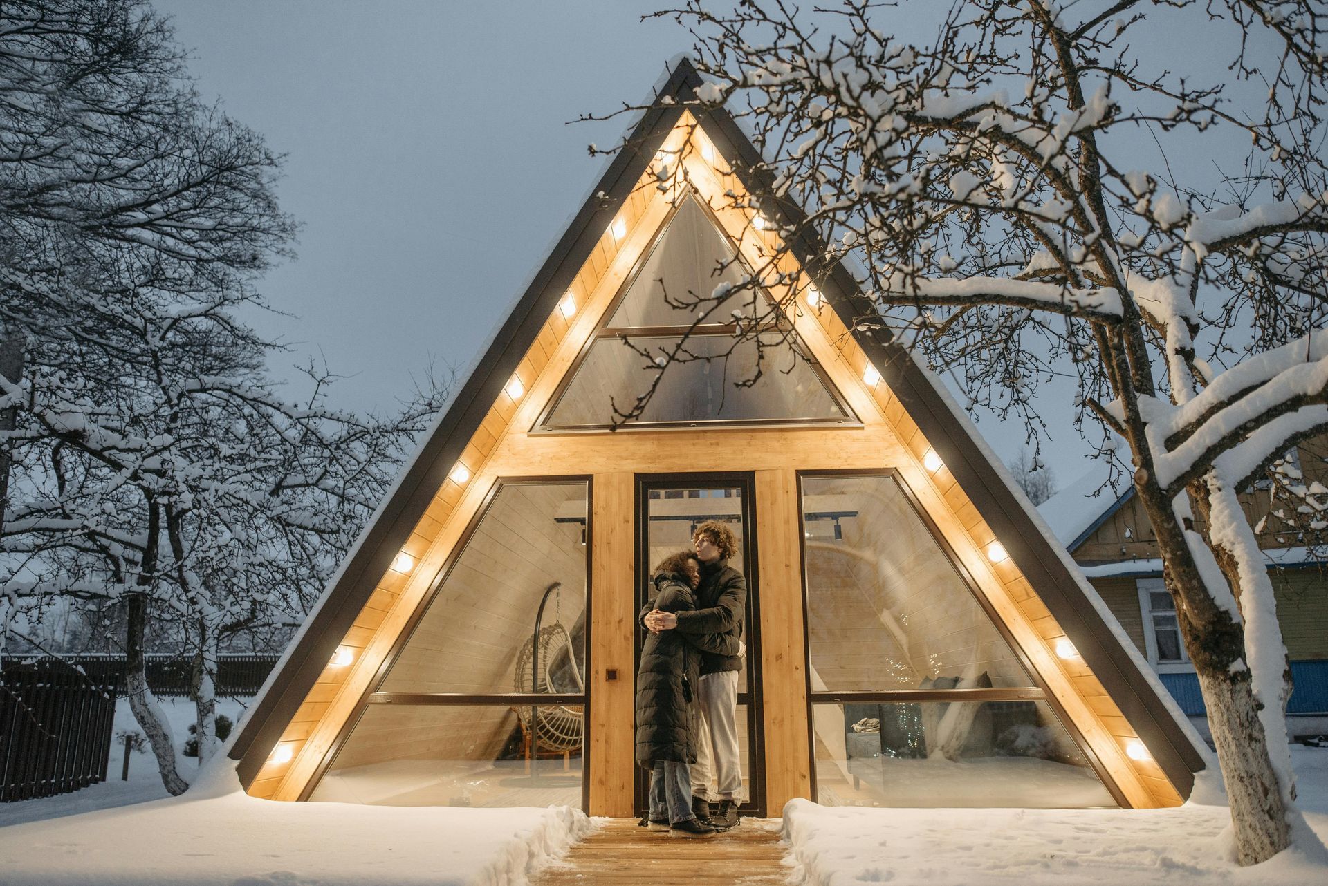 A couple is hugging in front of an a frame house in the snow.