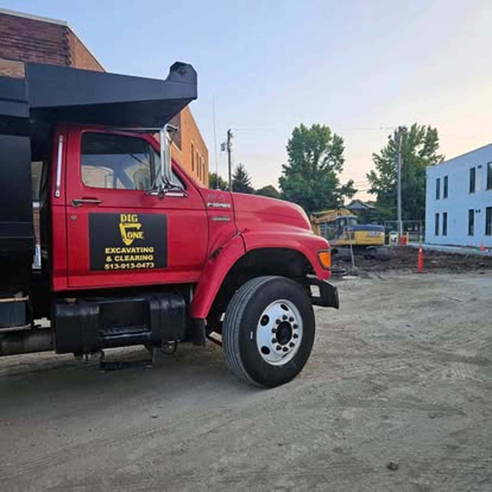 A red dump truck is parked in a dirt lot in front of a building.