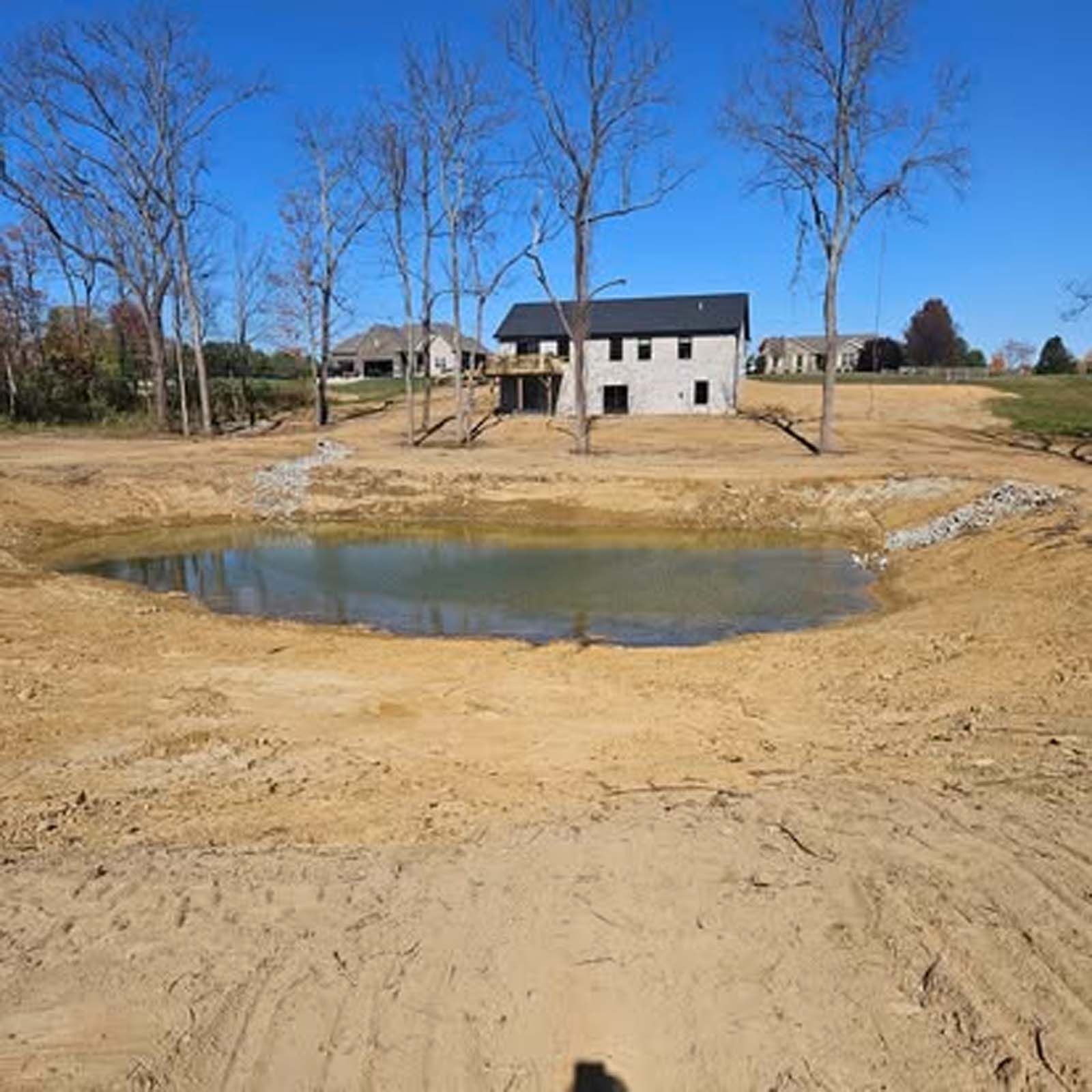 There is a pond in the middle of a dirt field in front of a house.
