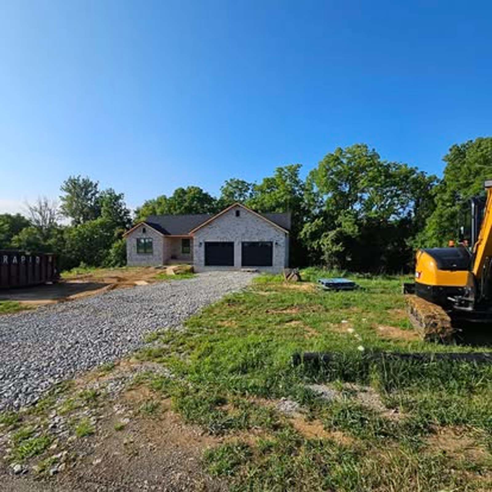 A yellow excavator is parked in front of a house under construction.