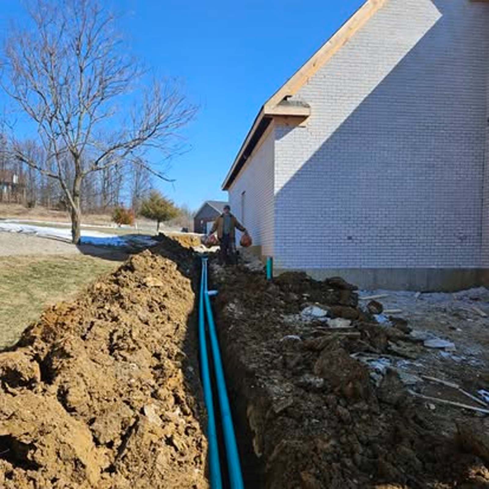 A man is digging a trench in front of a house.