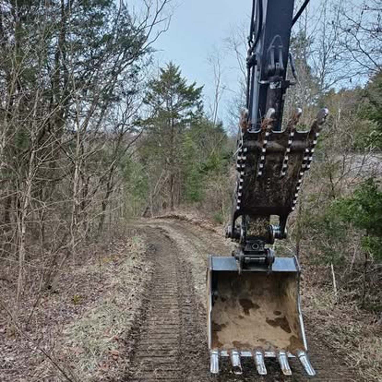 An excavator is digging a dirt road in the woods.
