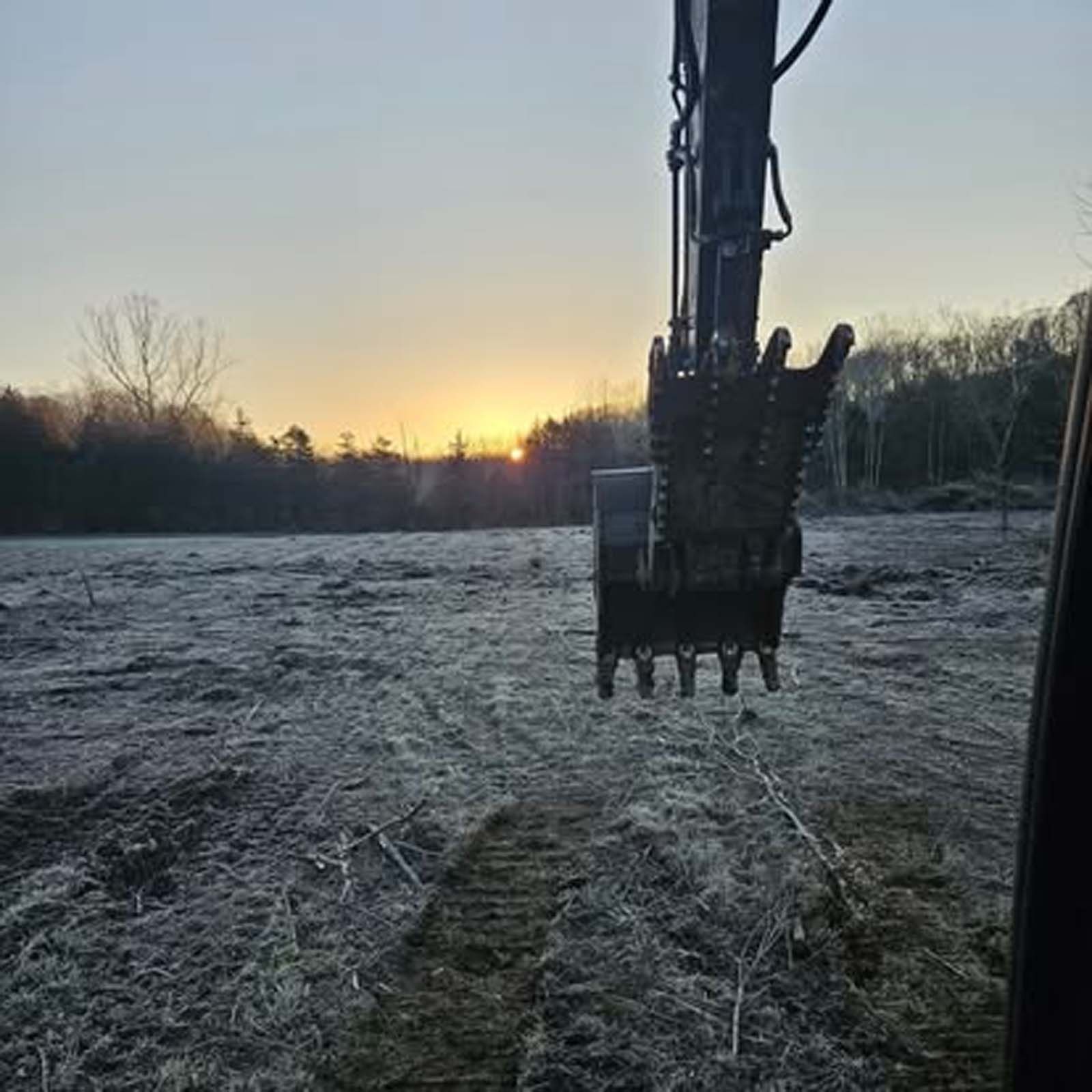 A bulldozer is digging a hole in a field at sunset.