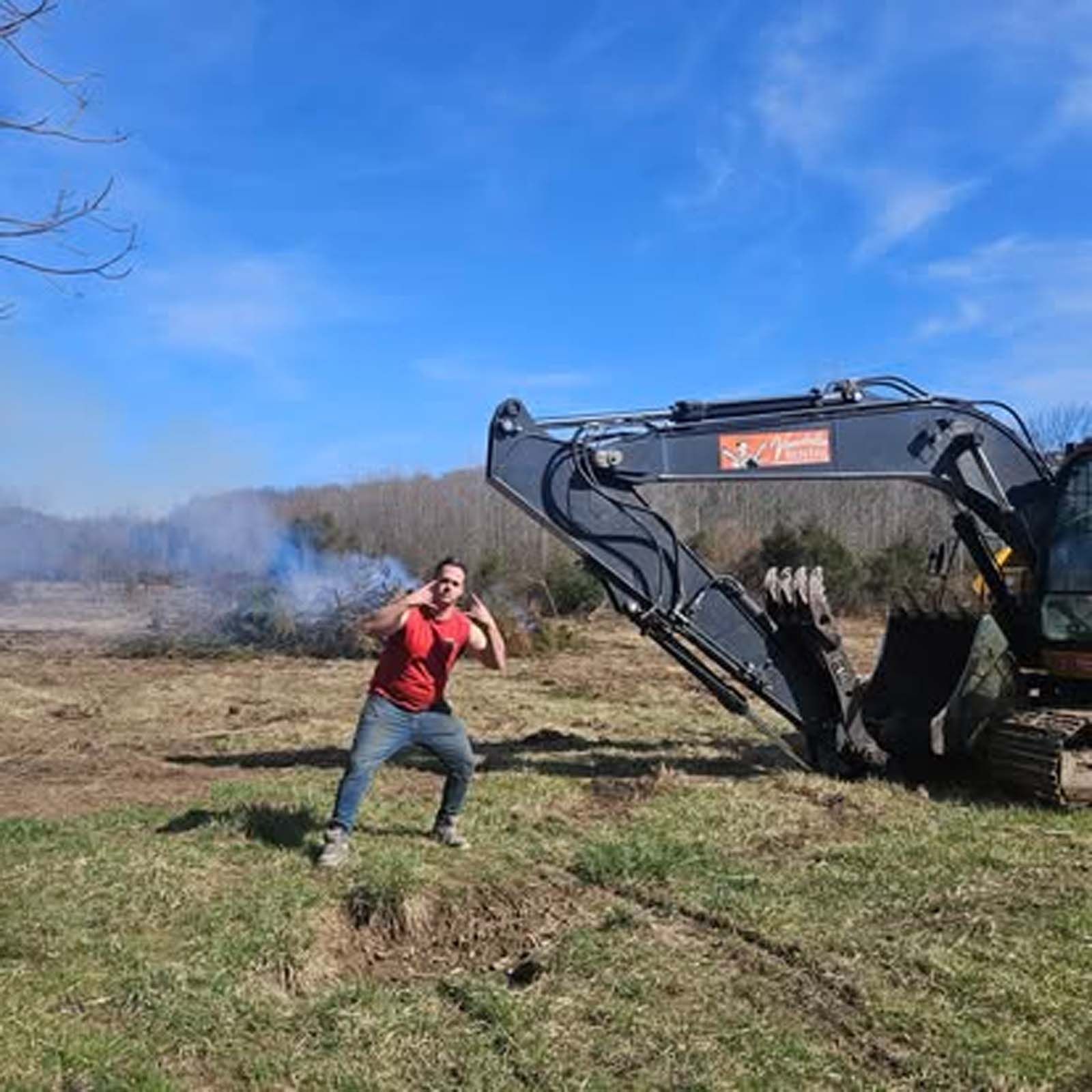 A man is standing in front of a large excavator in a field.