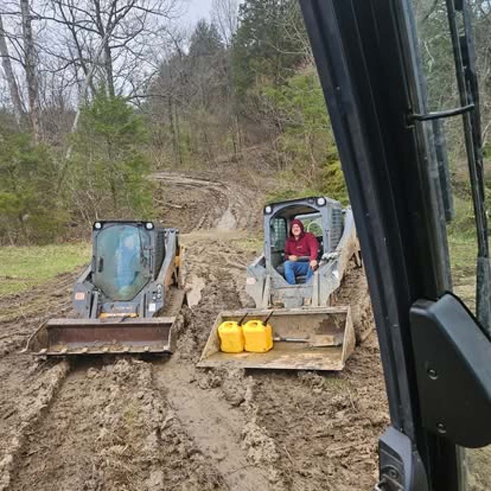 Two bulldozers are driving down a muddy road.