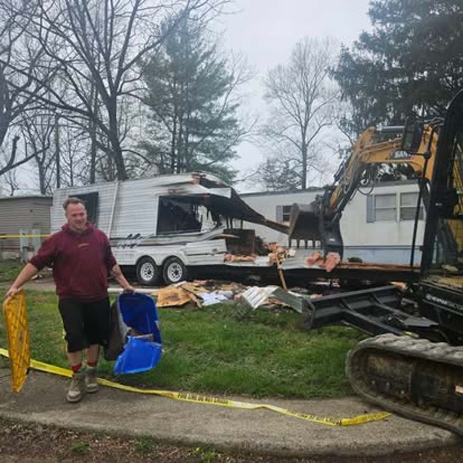 A man is standing in front of a trailer that has been demolished.