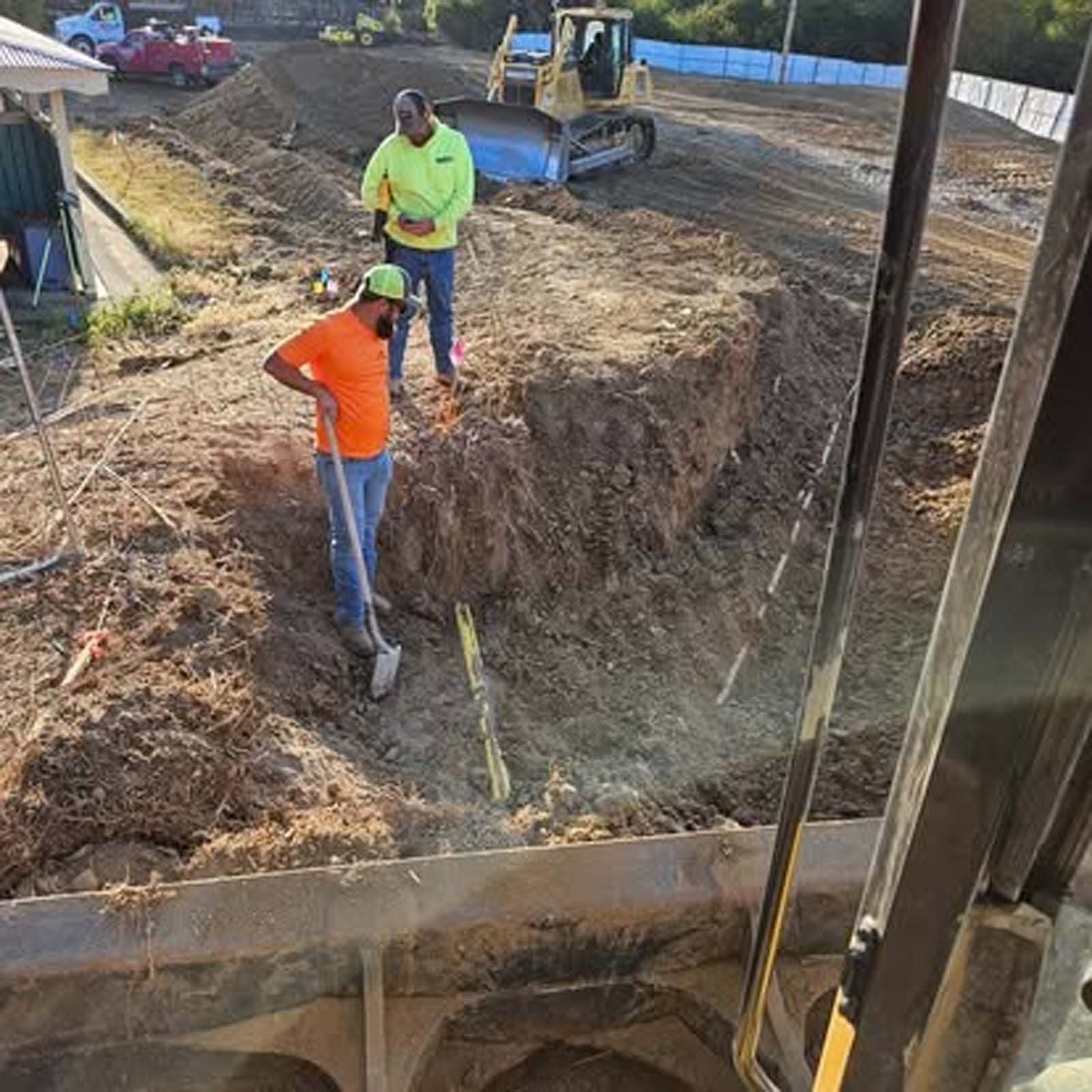 A man in an orange shirt is digging in the dirt with a shovel.