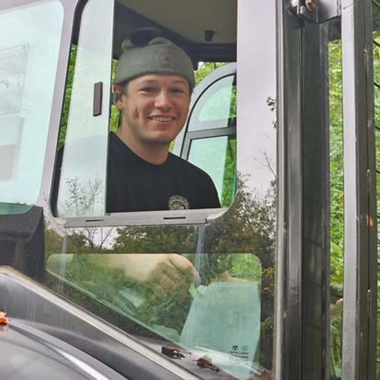 A man wearing a beanie is looking out the window of a truck.