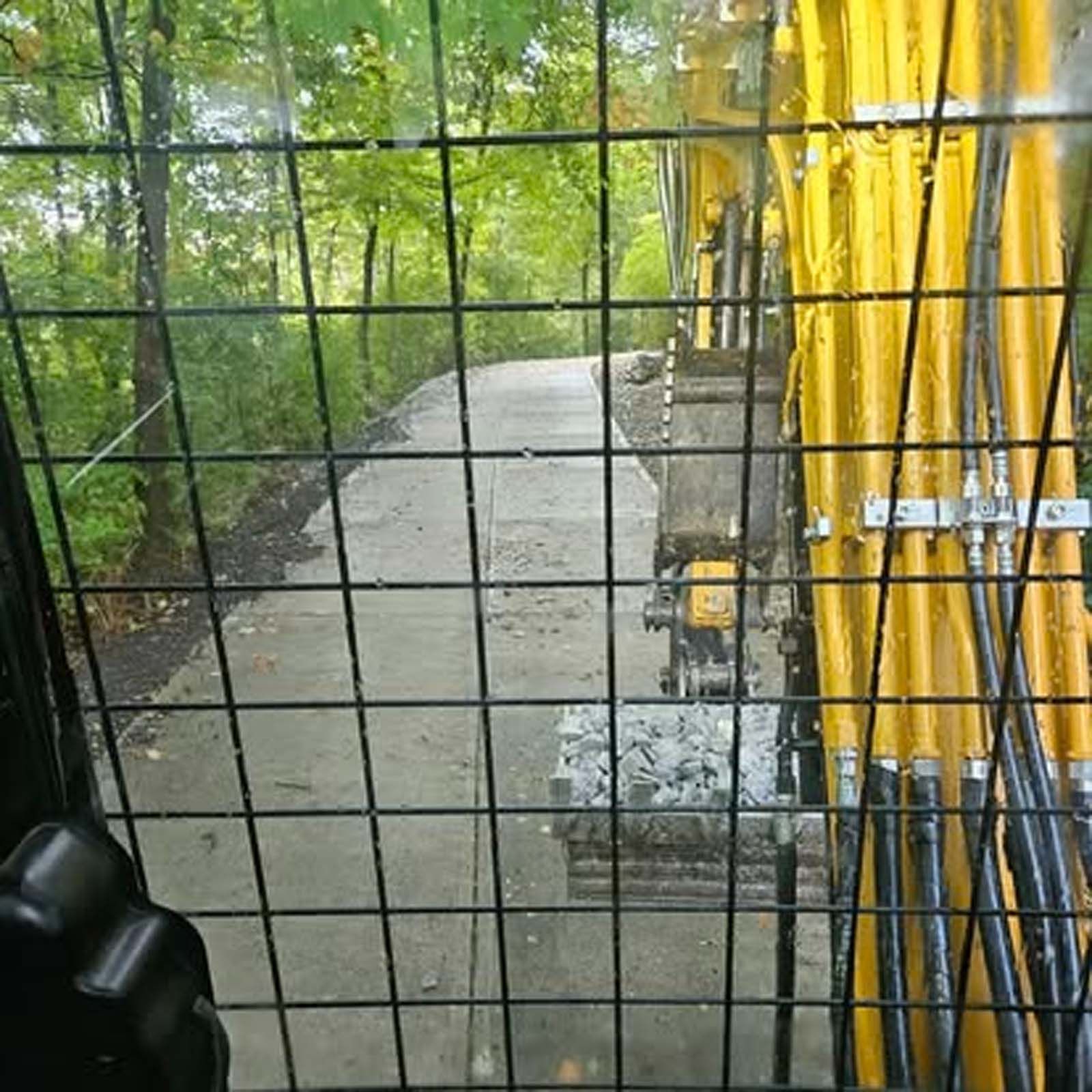 A yellow excavator is driving down a road behind a fence