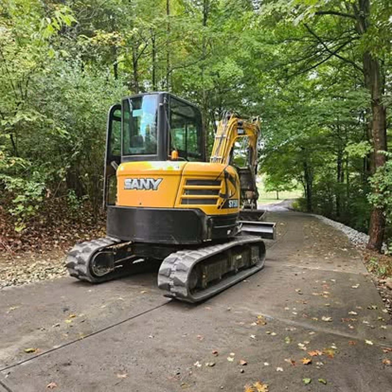 A yellow excavator is parked on the side of a road in the woods.