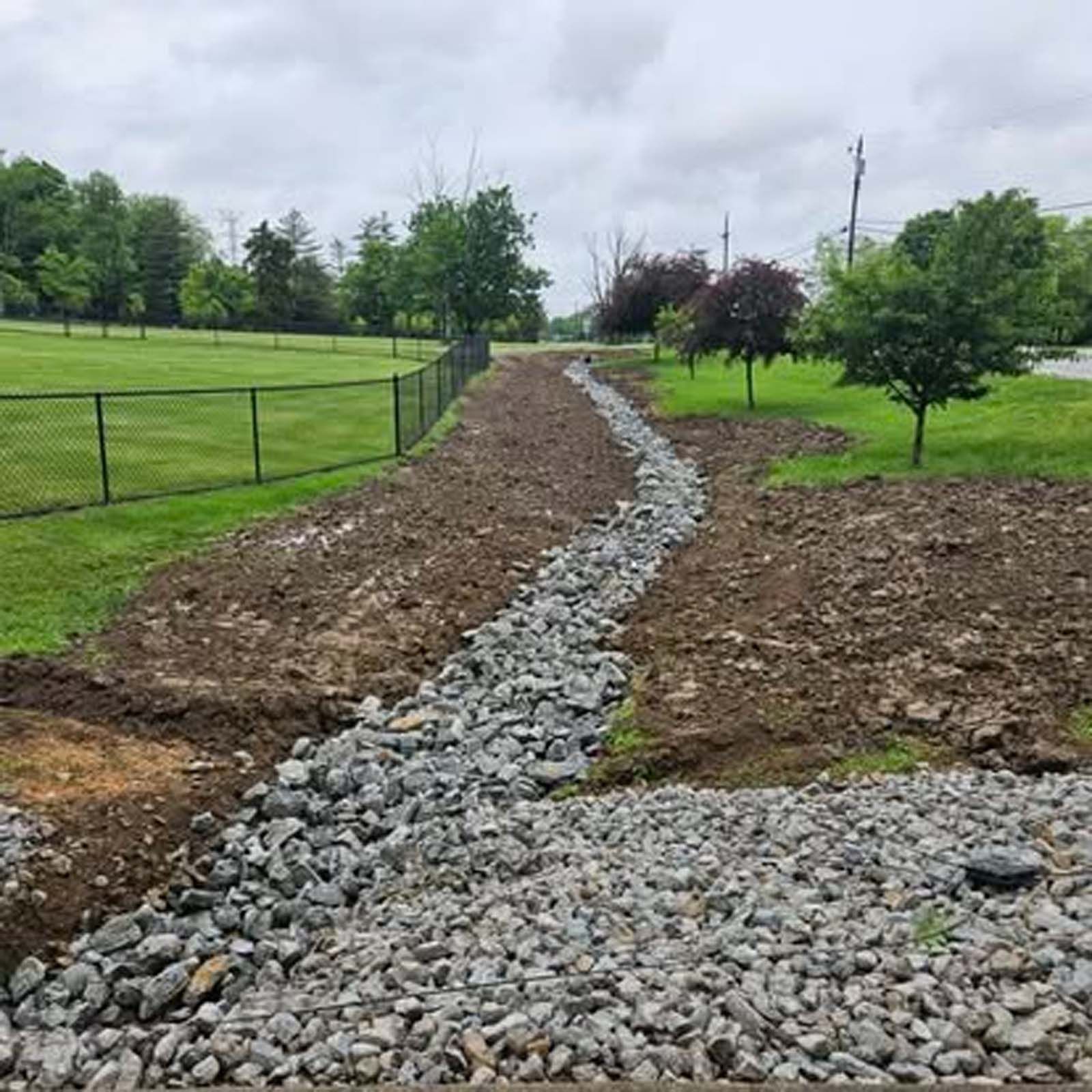 A gravel road going through a grassy field with a fence in the background.