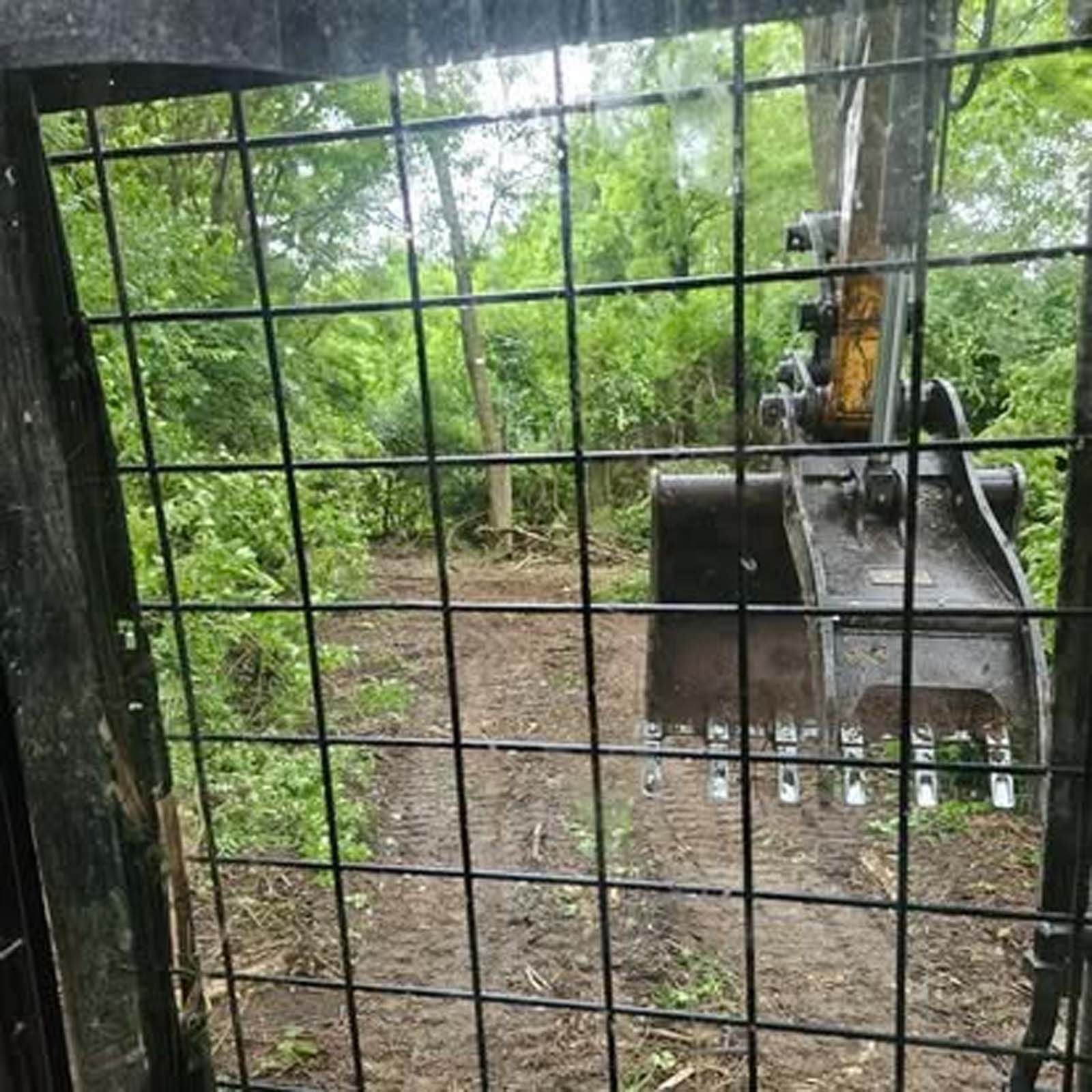 A fence with a view of an excavator in the woods behind it.