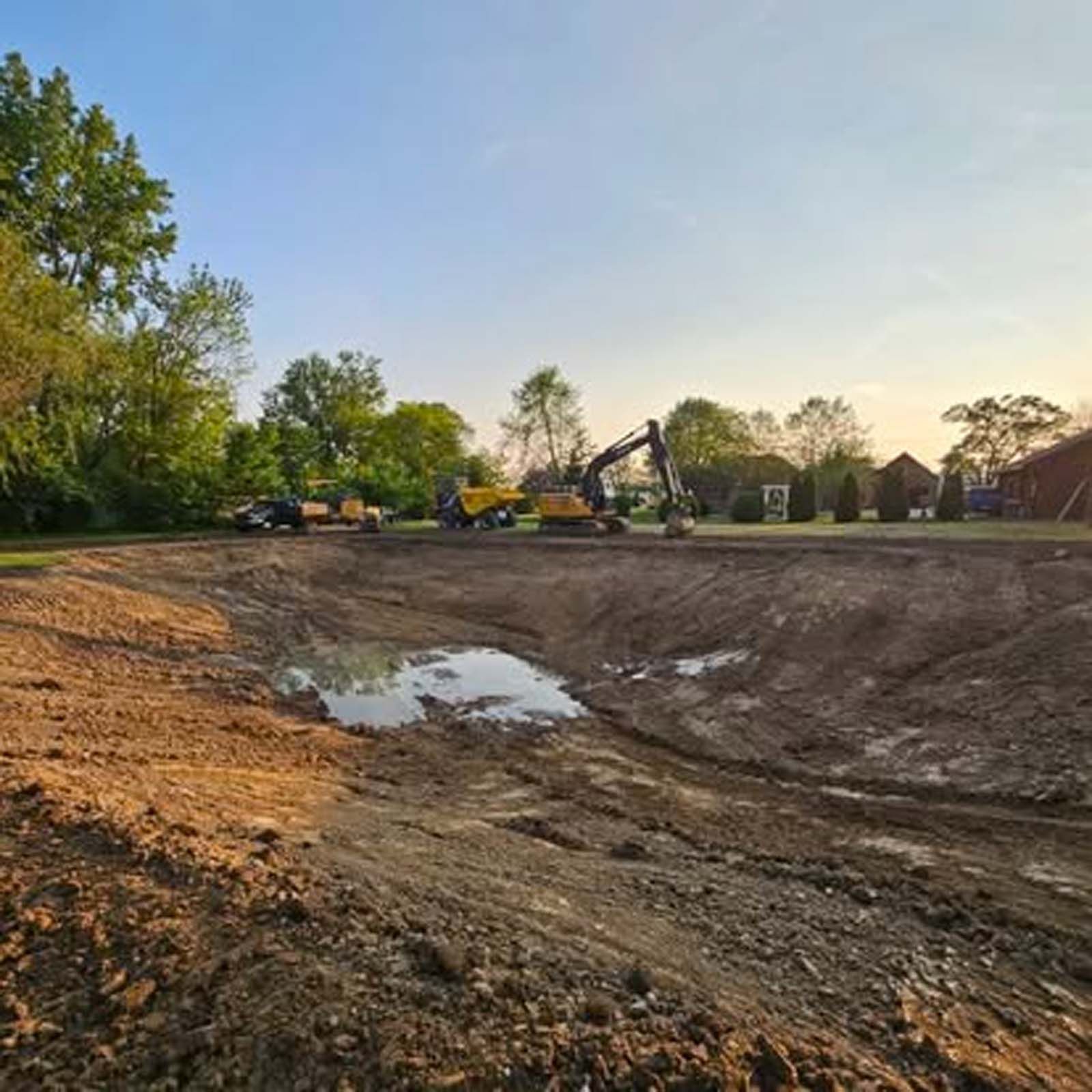 A yellow excavator is digging a hole in a dirt field.