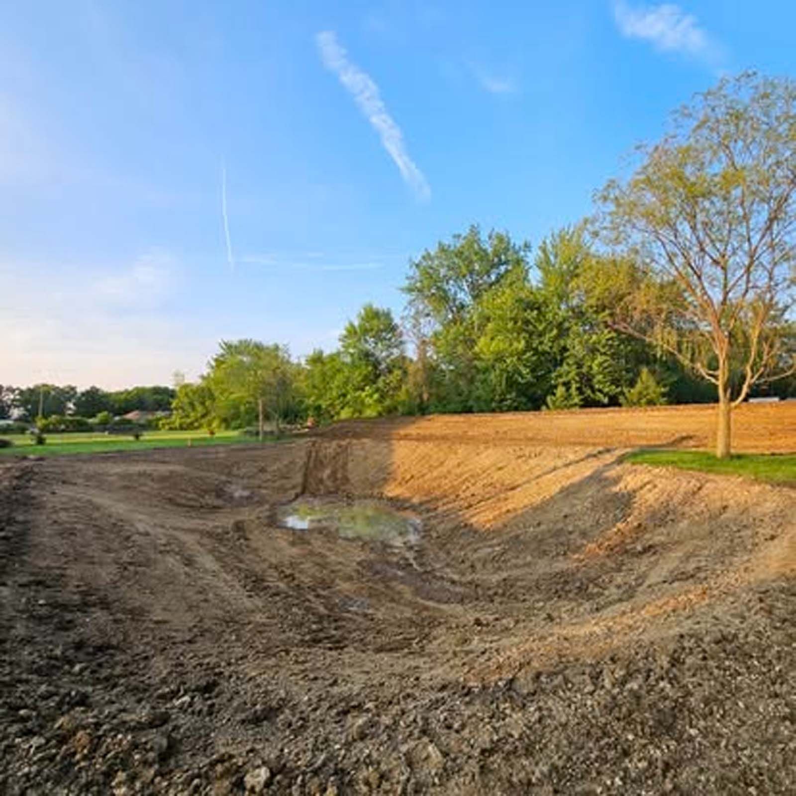 A large dirt field with trees in the background and a blue sky in the background.