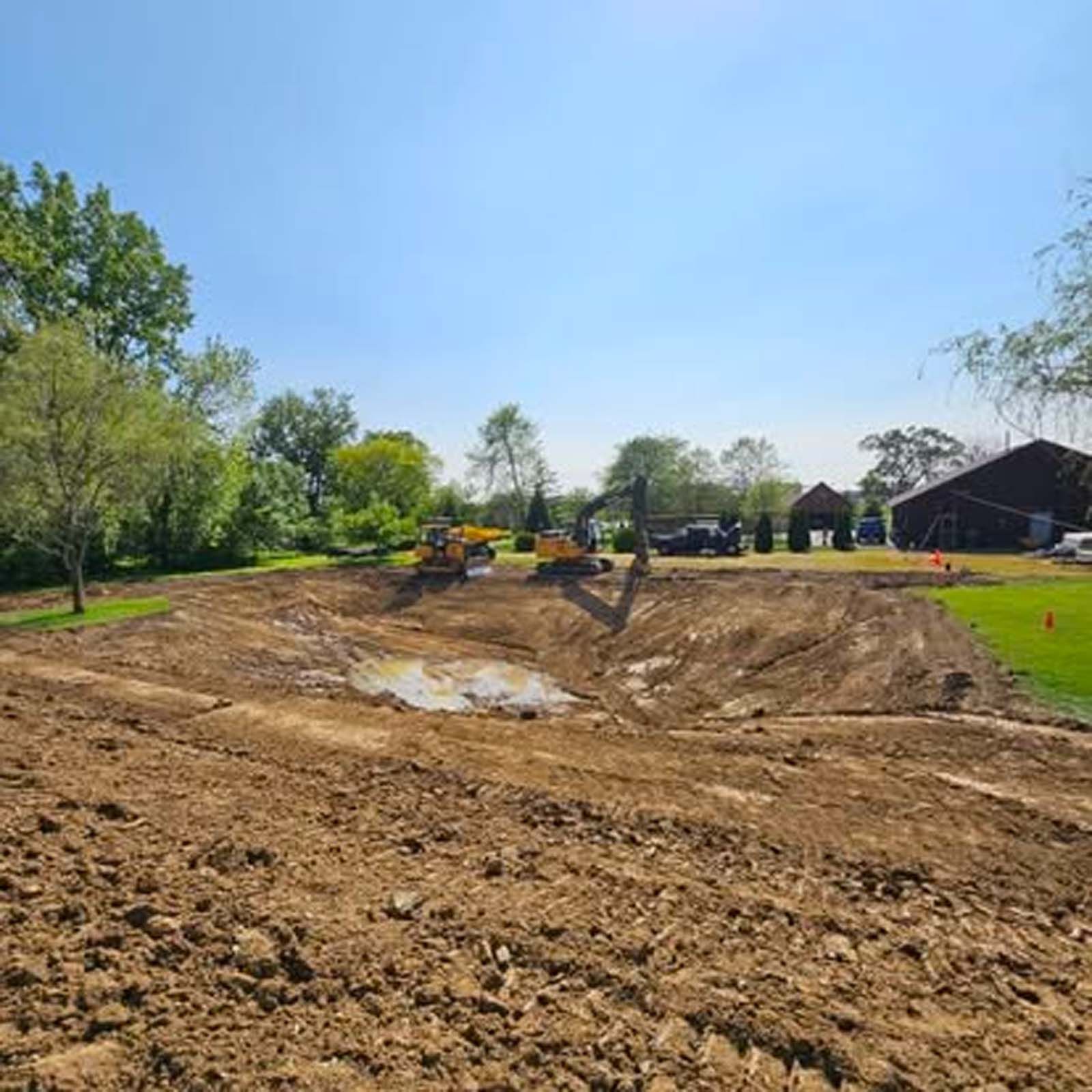 A large dirt field with a pond in the middle of it.