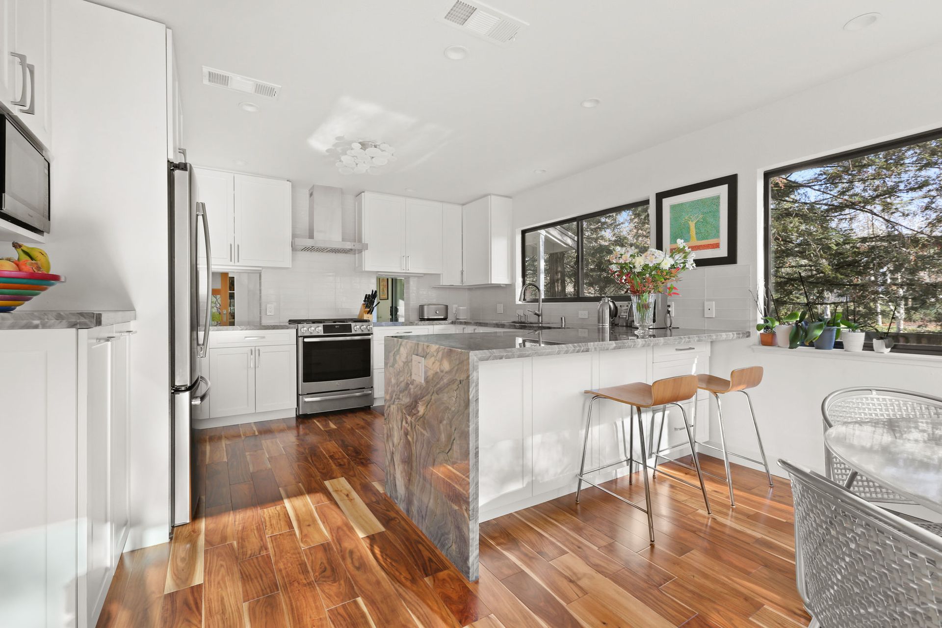 A kitchen with hardwood floors , white cabinets and stainless steel appliances.
