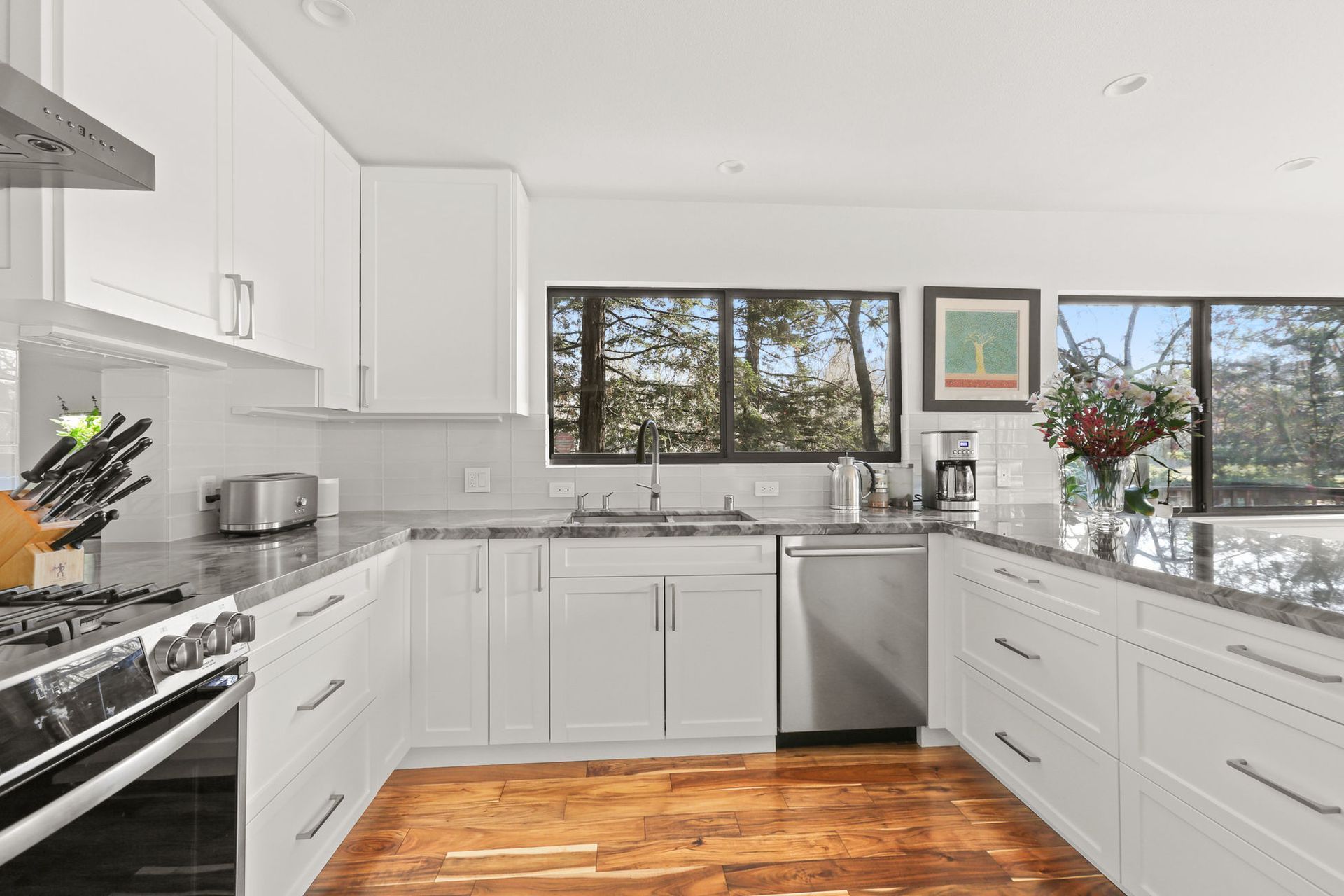A kitchen with white cabinets , stainless steel appliances , granite counter tops and hardwood floors.