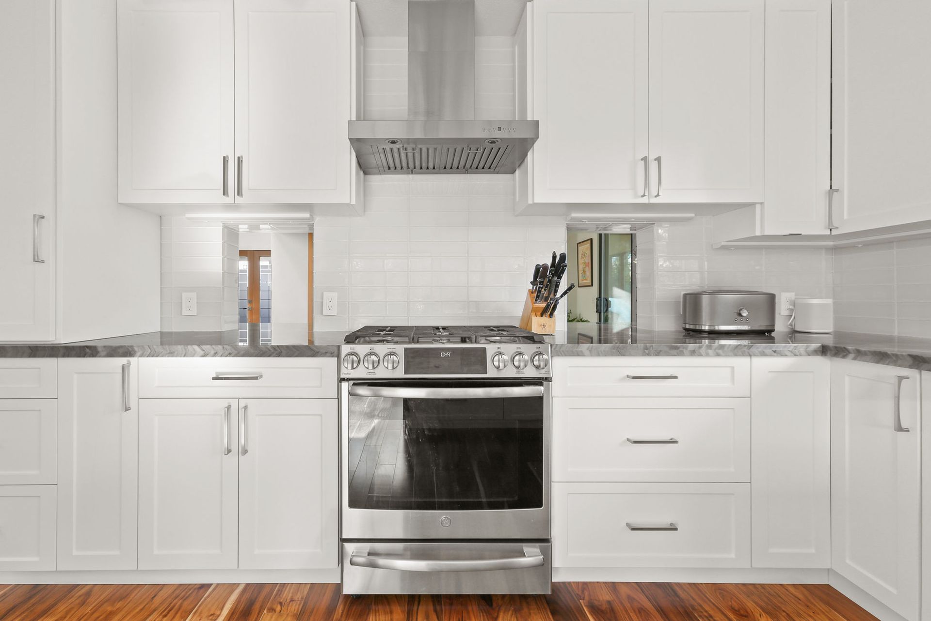 A kitchen with white cabinets , stainless steel appliances , and hardwood floors.