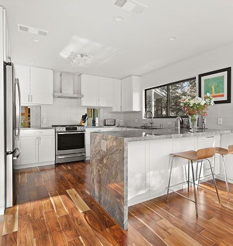 A kitchen with hardwood floors , white cabinets , stainless steel appliances and a large island.